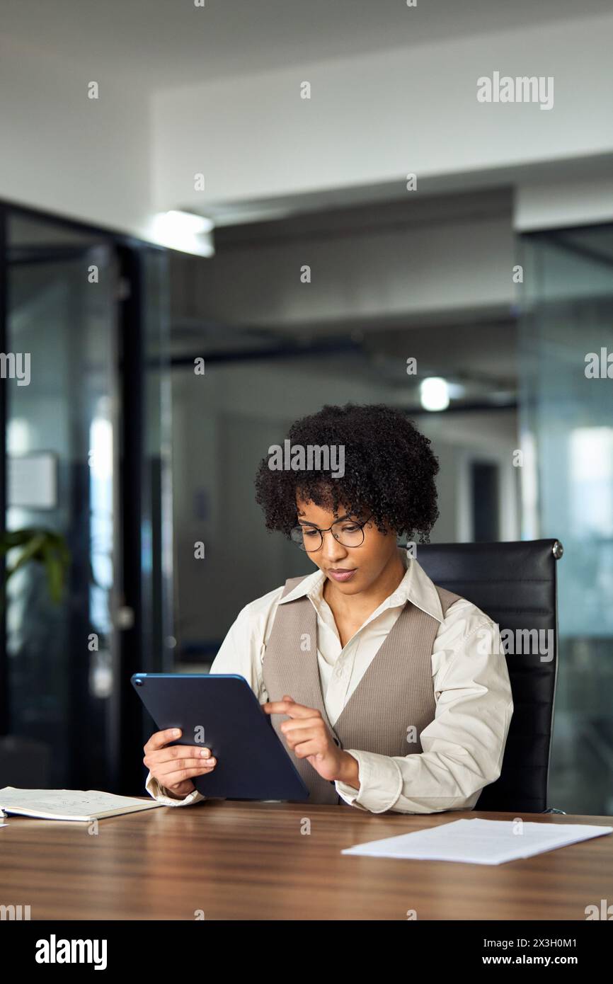 Young busy African business woman using tab working in office. Vertical. Stock Photo