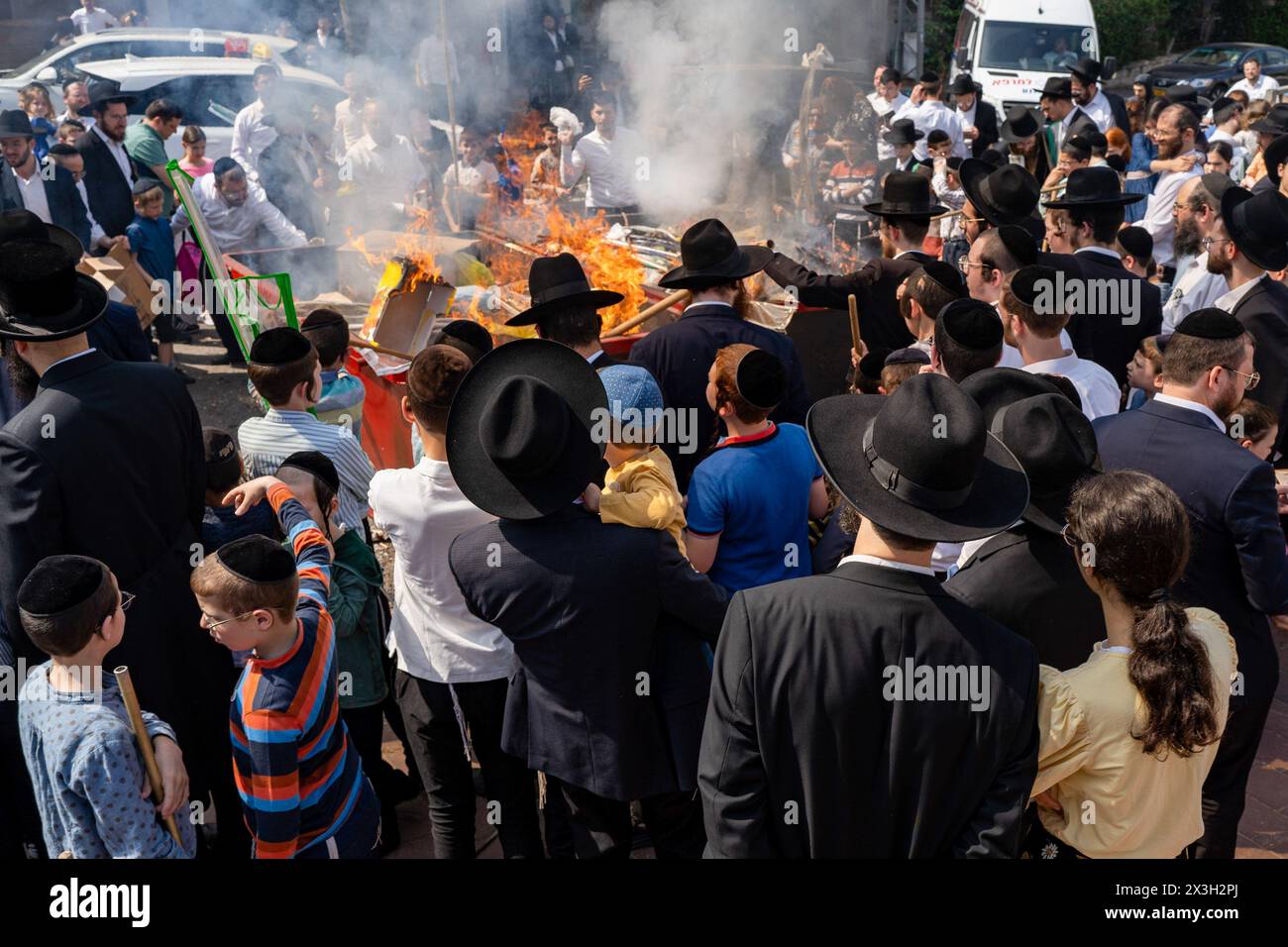 The Jewish Orthodox gather around the fire set to burn the leaven during the Biur Chametz. During the Biur Chametz, religious Jews fulfill their obligation to inspect their homes for any leaven and eliminate it before the night of Passover. In ultra-Orthodox cities in Israel, fires are set up in major locations in the city for this purpose, where people bring their bread leftovers to burn the leaven. During the seven days of Passover, they are prohibited from eating or possessing any leaven, symbolizing the dough the Israelites did not have time to allow to rise before the Exodus from Egypt. B Stock Photo