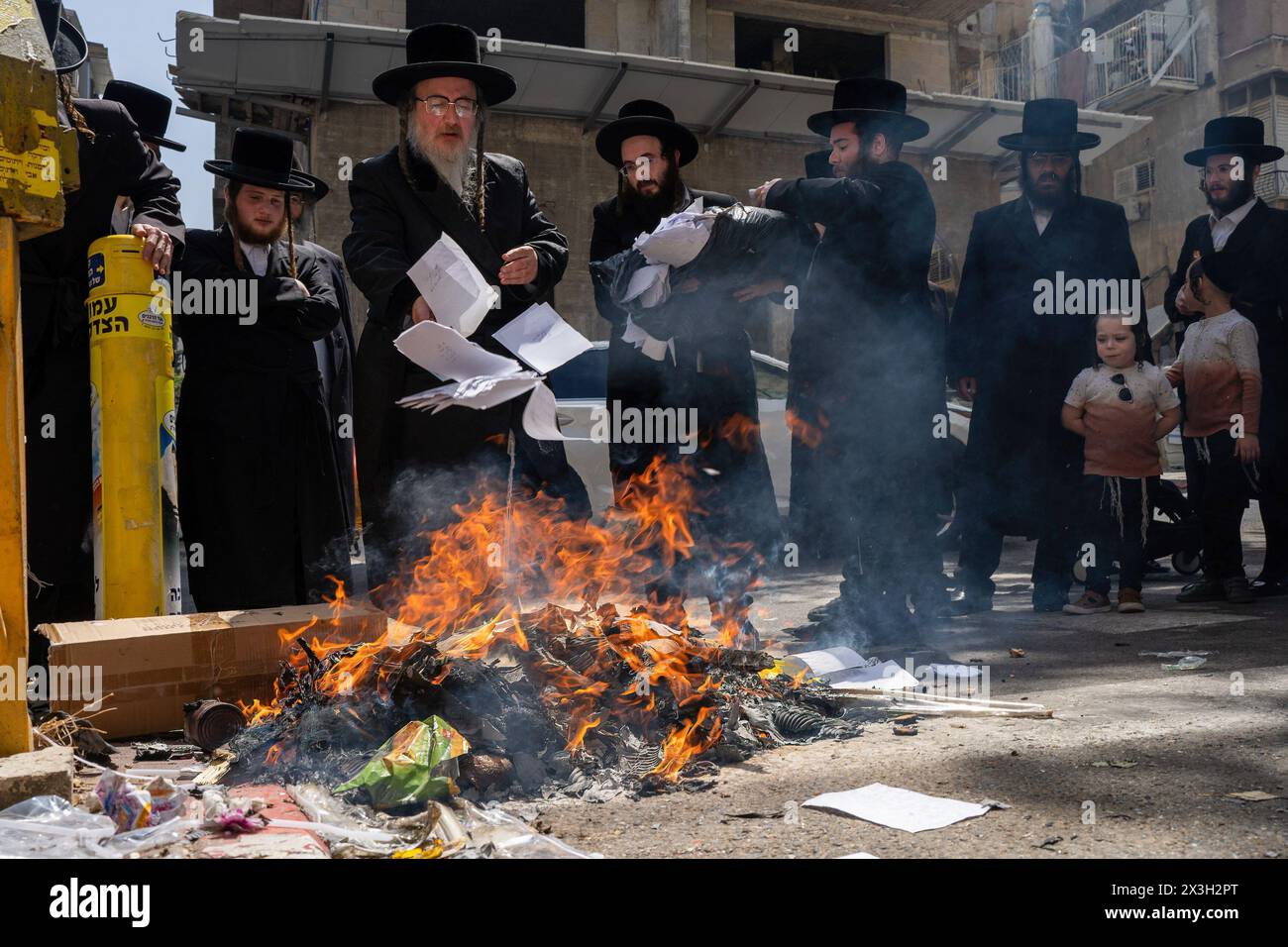 A Jewish Rabbi is seen throwing papers to the fire. During the Biur Chametz, religious Jews fulfill their obligation to inspect their homes for any leaven and eliminate it before the night of Passover. In ultra-Orthodox cities in Israel, fires are set up in major locations in the city for this purpose, where people bring their bread leftovers to burn the leaven. During the seven days of Passover, they are prohibited from eating or possessing any leaven, symbolizing the dough the Israelites did not have time to allow to rise before the Exodus from Egypt. Biur Chametz, also known as 'the burning Stock Photo