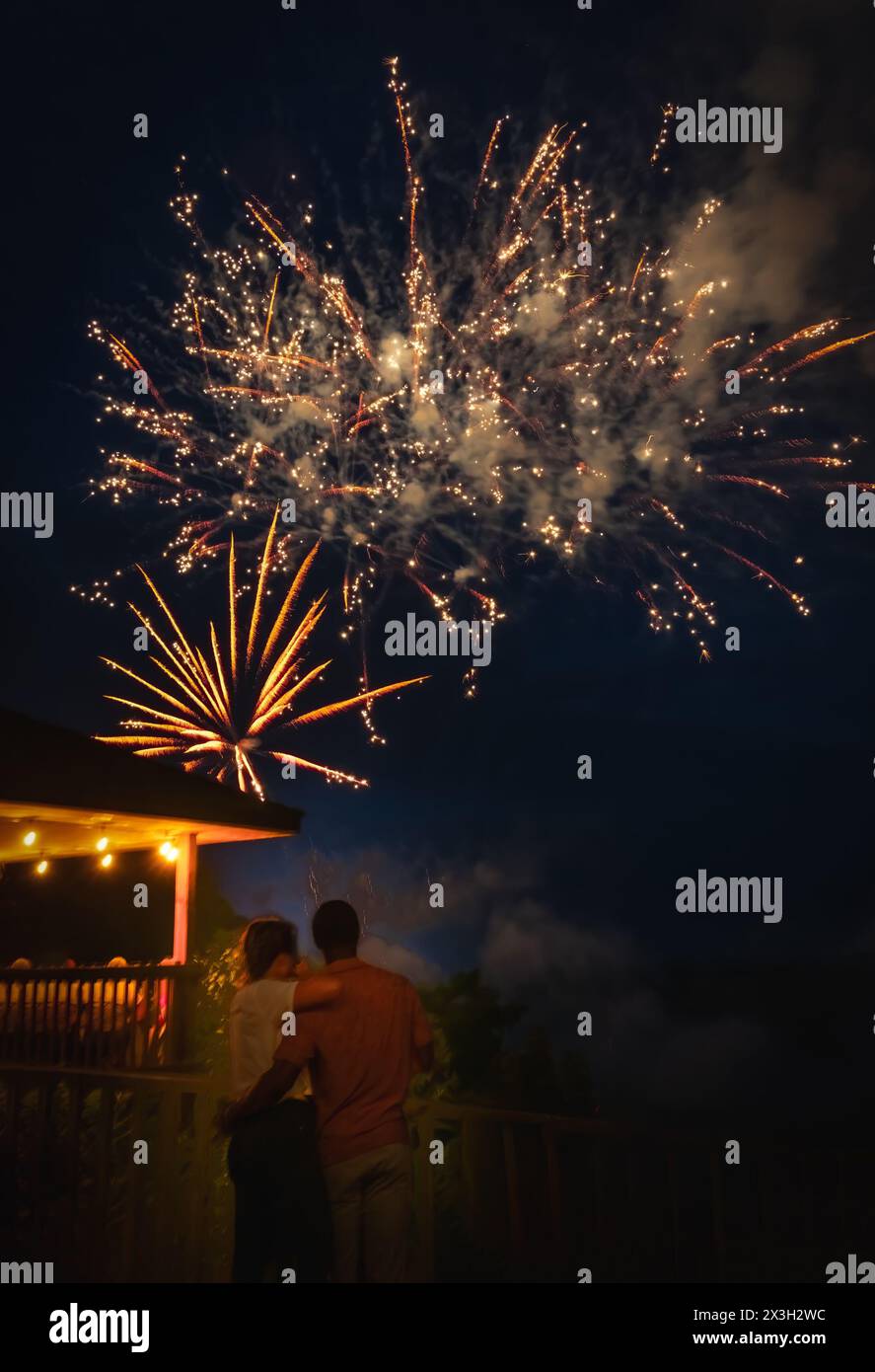 Young African American man hugging his white girlfriend while watching Fourth of July fireworks from observation deck over river Stock Photo
