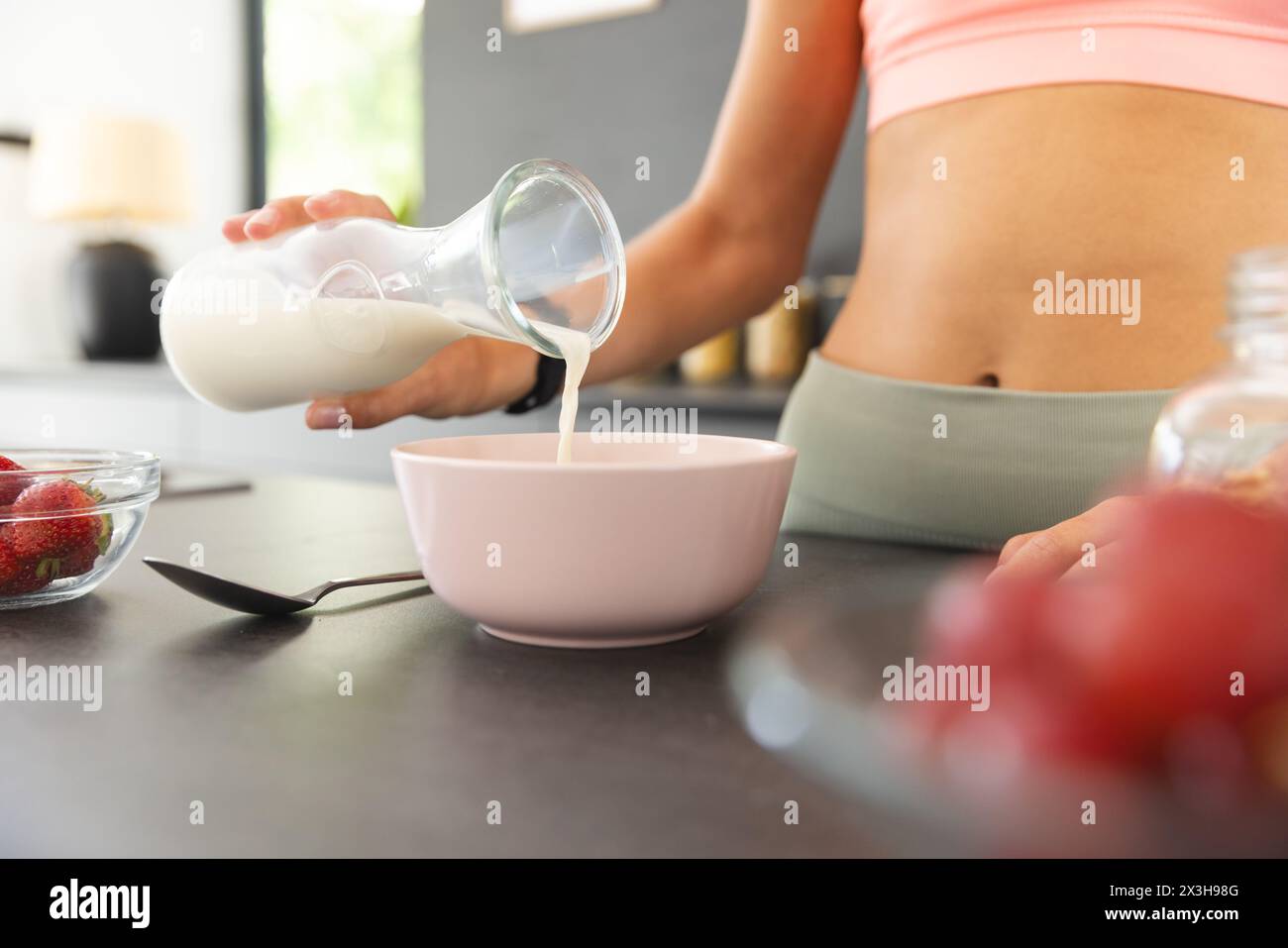 A young Caucasian woman at home, wearing pink crop top, pouring milk into a bowl Stock Photo