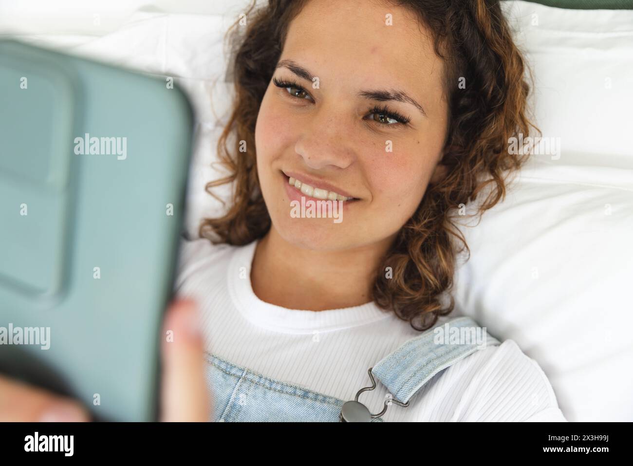 A young Caucasian woman holding smartphone, lying on bed at home Stock Photo