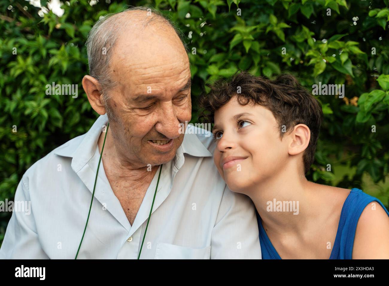 Grandfather and grandson enjoying a shared laugh in a serene garden - Elderly man and a young boy gazing in a tender moment, surrounded by lush greene Stock Photo