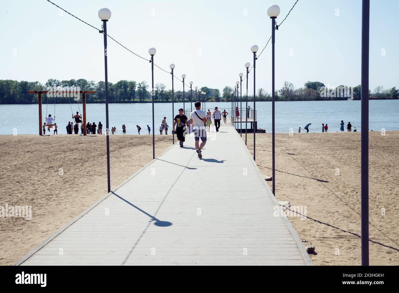 pier on public city beach of lake with people on sunny day. pleasure observation pier, leisure activity. Creation of urban comfortable landscape desig Stock Photo