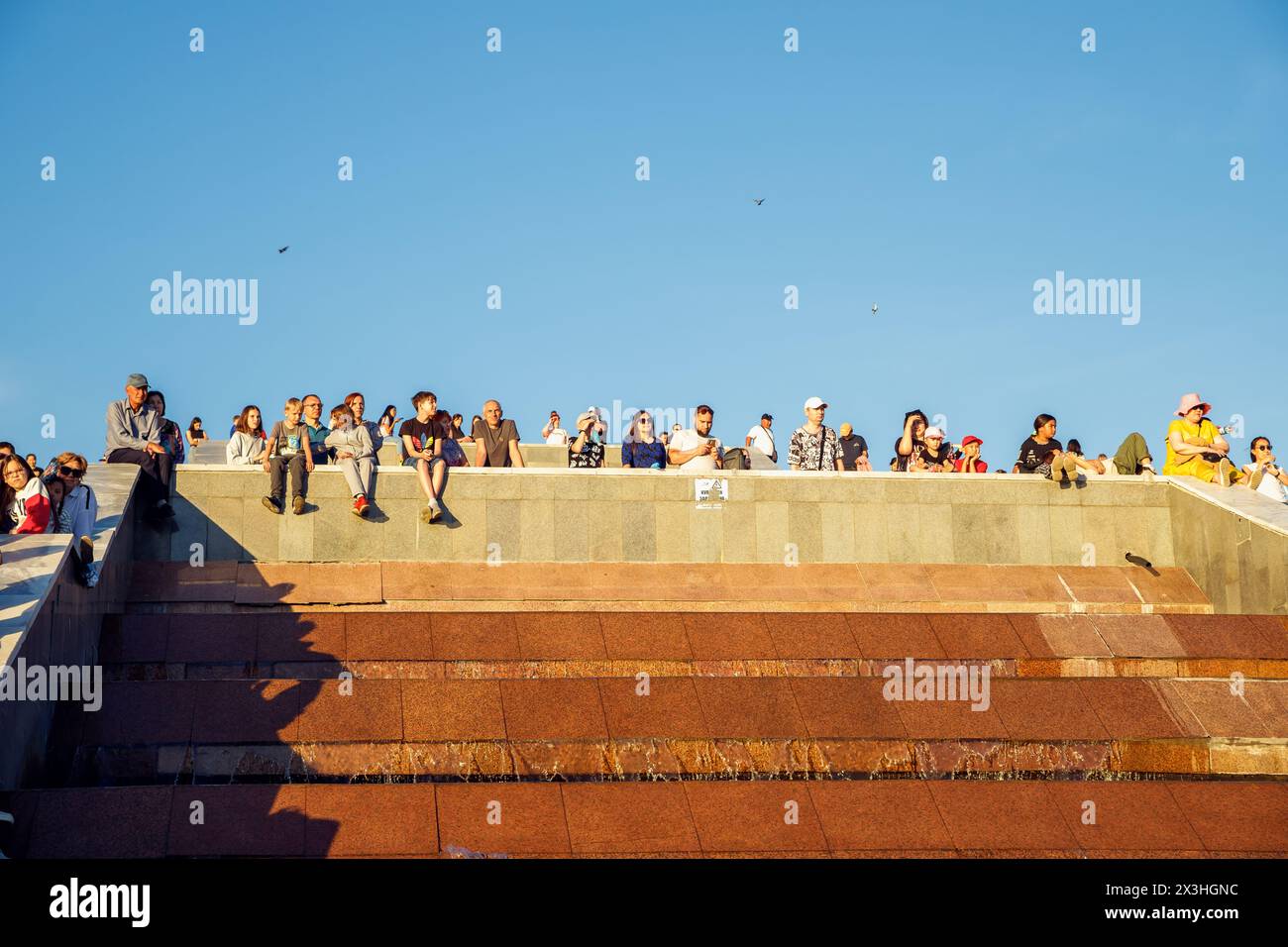 people sit on city fountain and watch celebration on National city day on blue sky. Pavlodar, Kazakhstan - 9.7.2023. Weekend Stock Photo