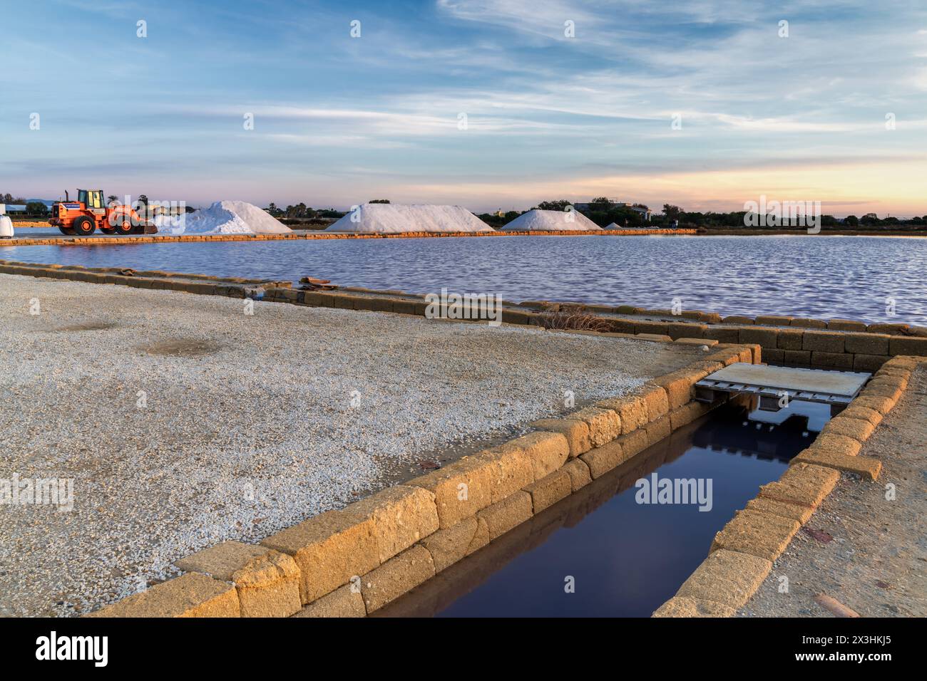 Paceco, Italy - 3 January, 2024: front loader and piles of sea salt in the salt flat of Trapani and Paceco at sunset Stock Photo