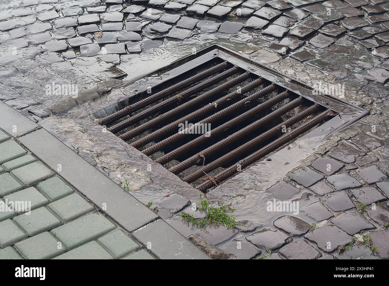 Water flows down through the manhole cover on a runny day Stock Photo