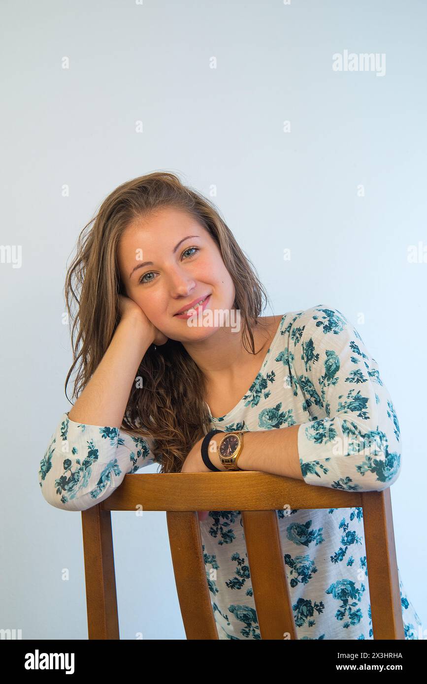 Young woman sitting astride, smiling, head on hand. Stock Photo