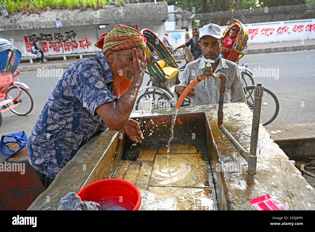 A rickshaw driver washing his face with water at a roadside water ...