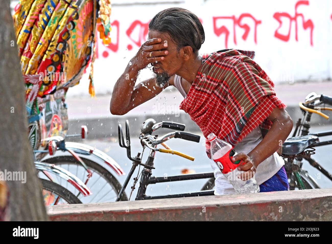 A rickshaw driver washing his face with water at a roadside water ...