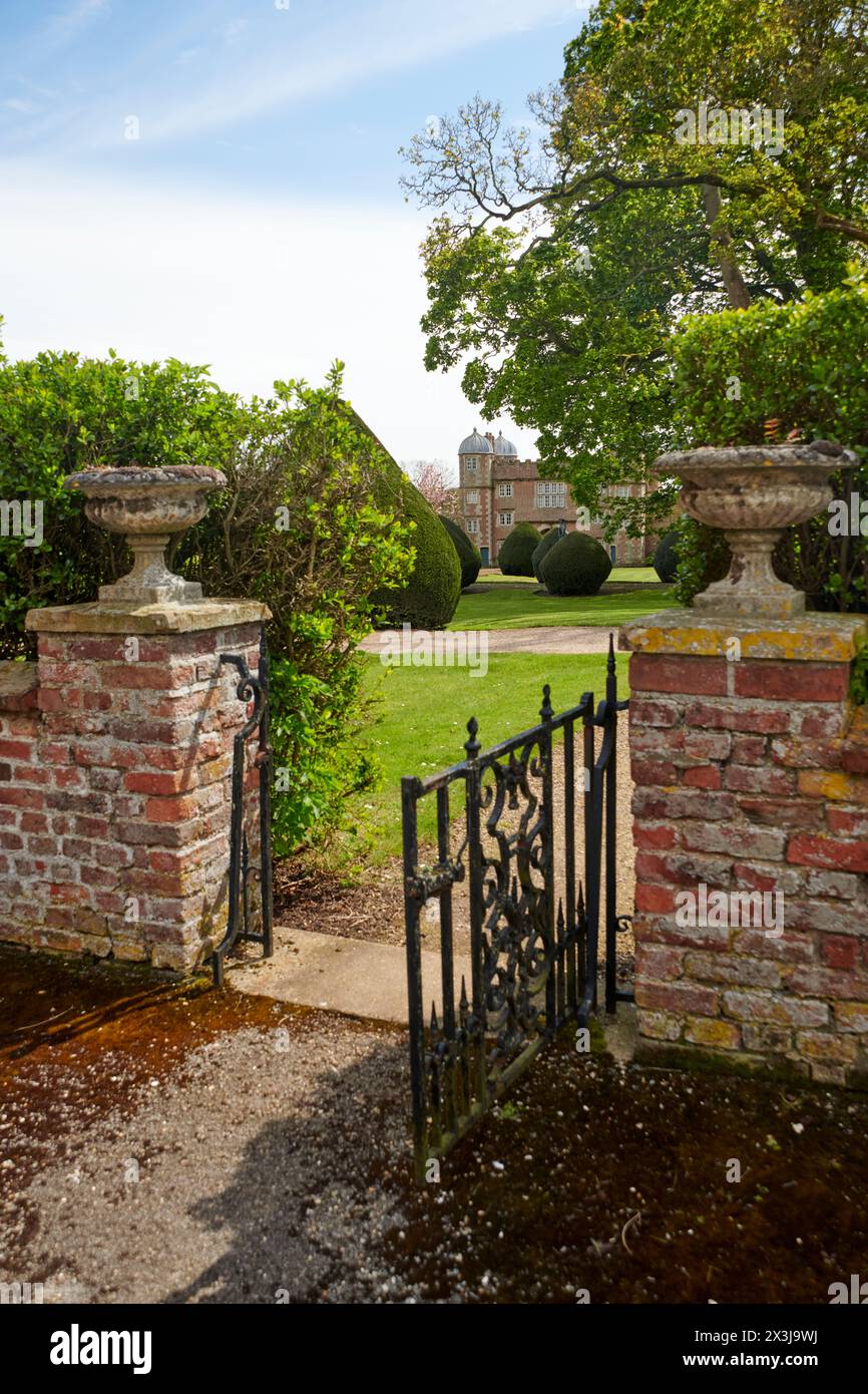Iron gate partially open leading to a traditional English country house with a landscaped garden Stock Photo
