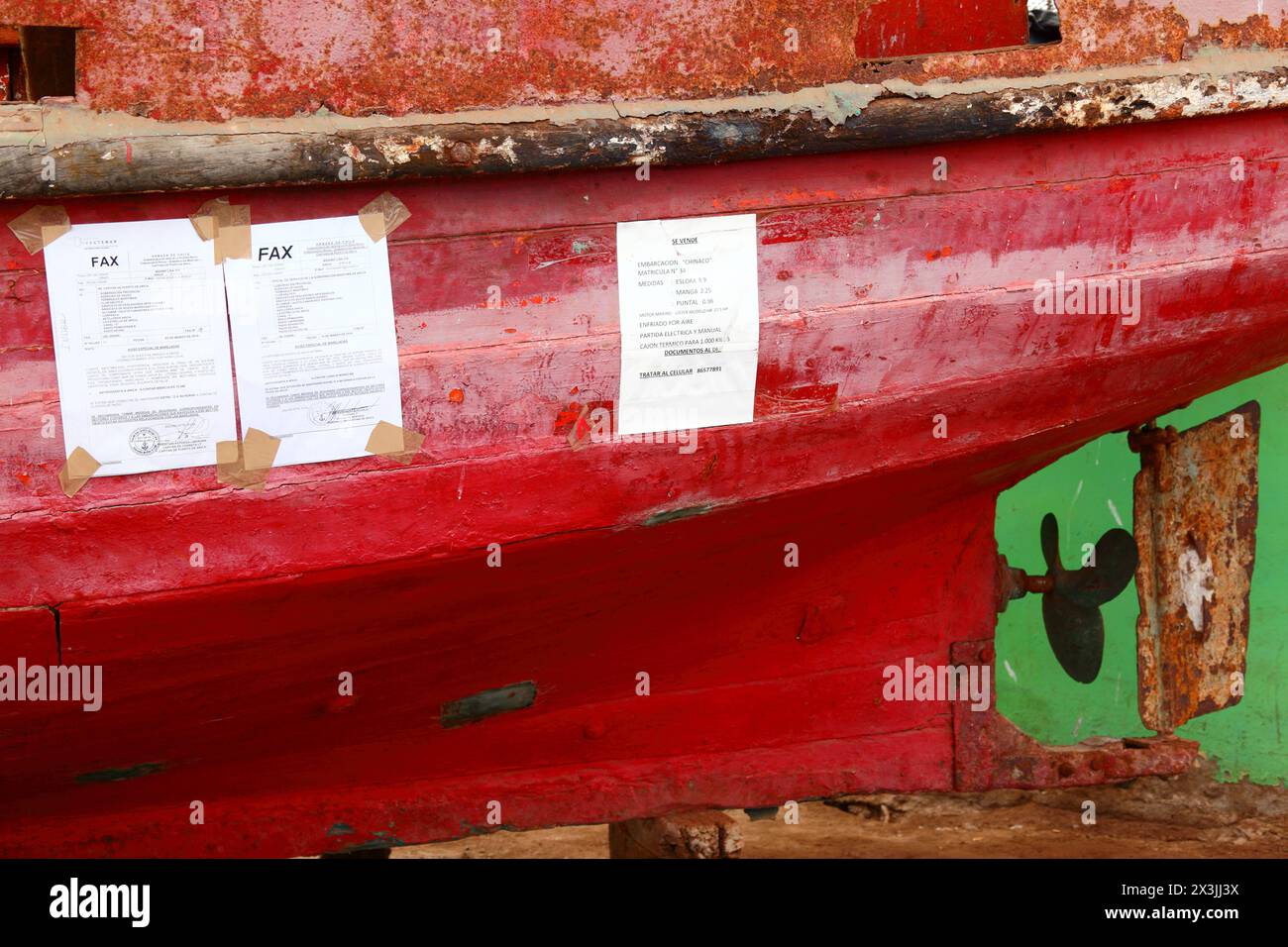 Printed faxes with warnings from Chilean Navy about bad weather and storm surges taped to side of old wooden fishing boat in port, Arica, Chile Stock Photo