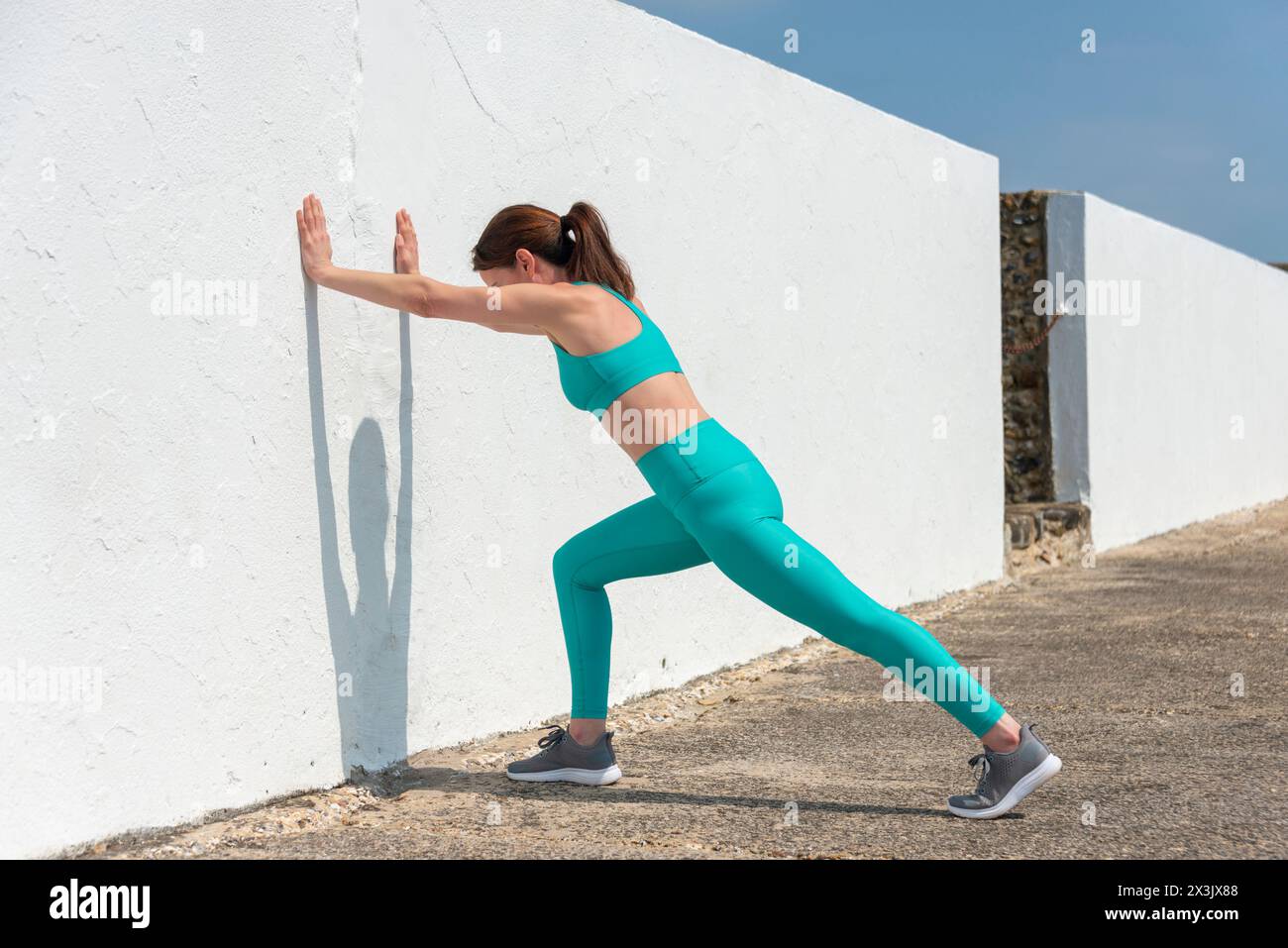 Sporty woman pushing against a white wall, warm up exercises. Stock Photo