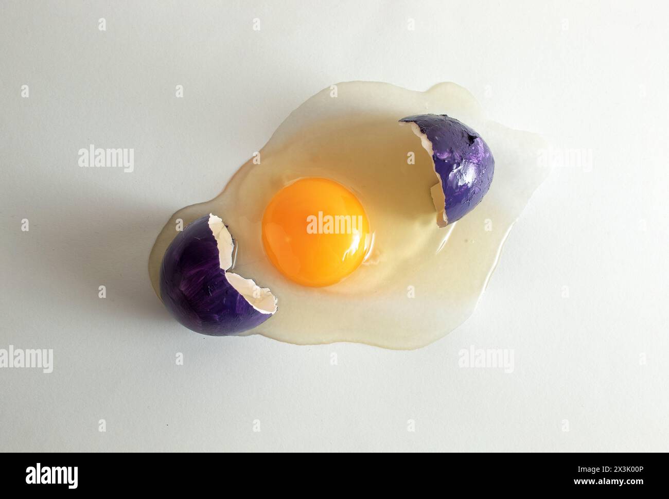 Cracked purple eggshell with raw egg. Creative copy space on light background. Minimal Easter concept. Stock Photo