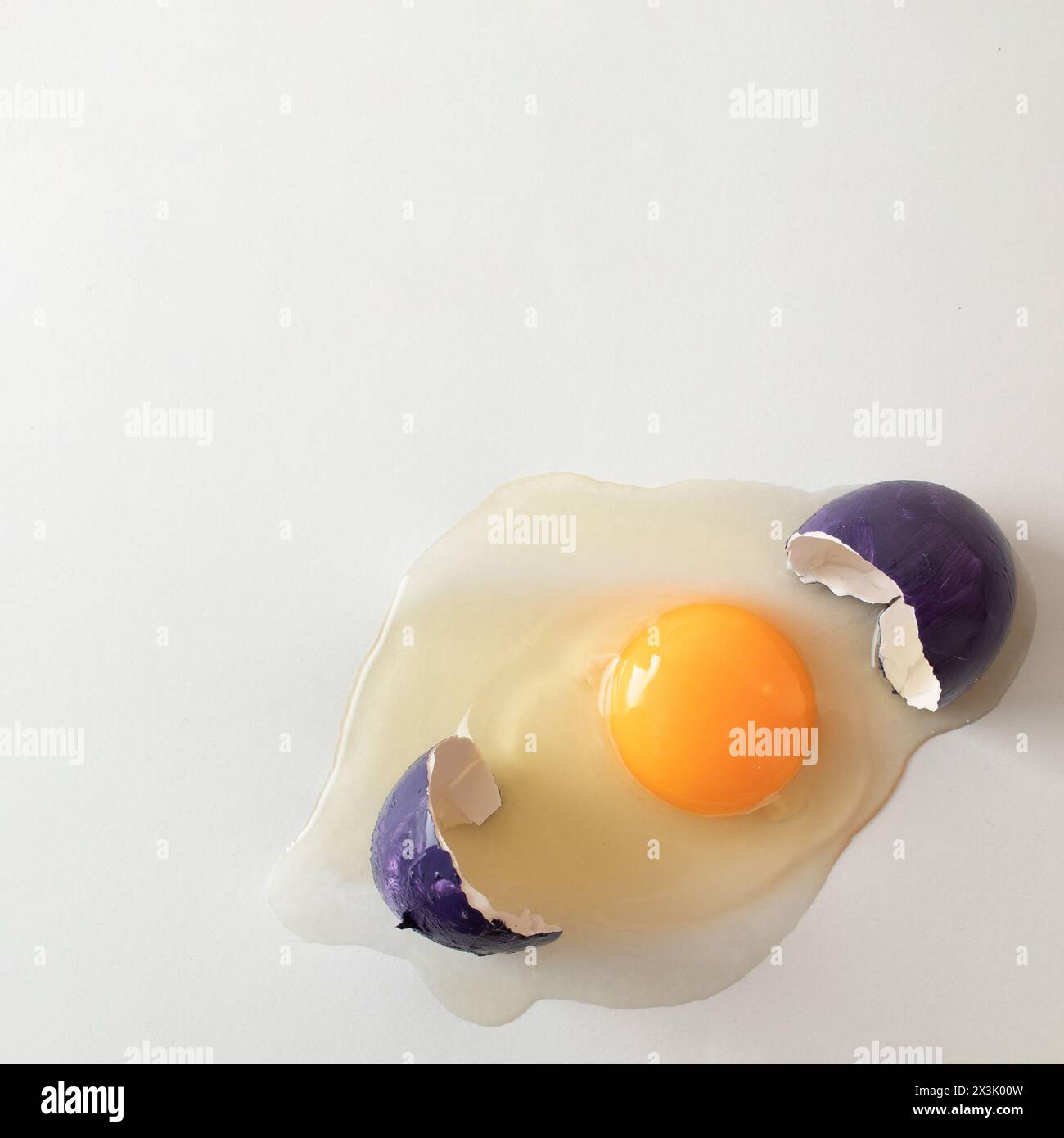 Cracked purple eggshell with raw egg. Creative copy space on light background. Minimal Easter concept. Stock Photo