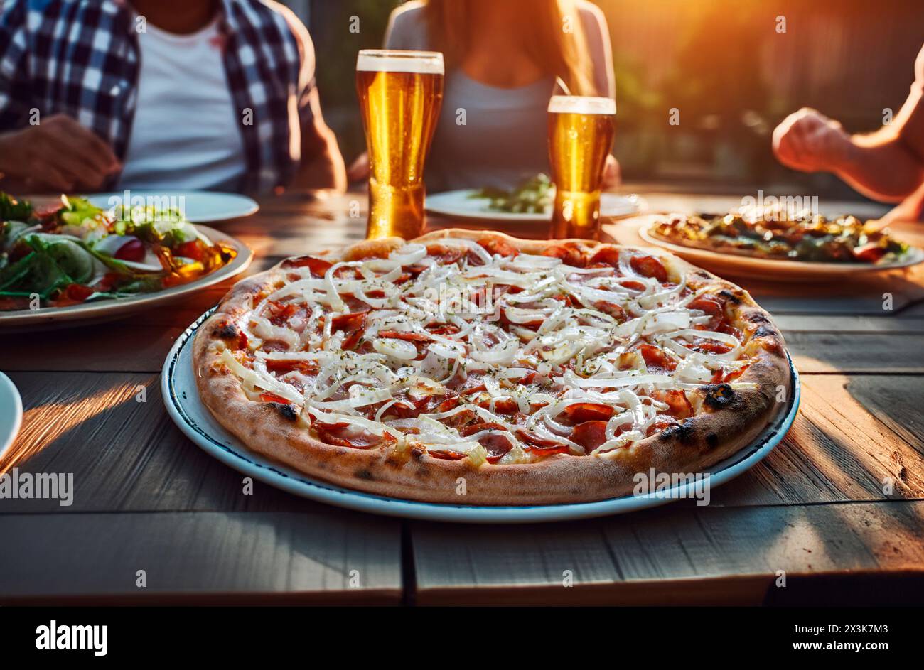 Colleagues or friends eat pizza and chat in a cafe. Leisure, food and drink, people and holidays concept, Pepperoni pizza with onion rings Stock Photo