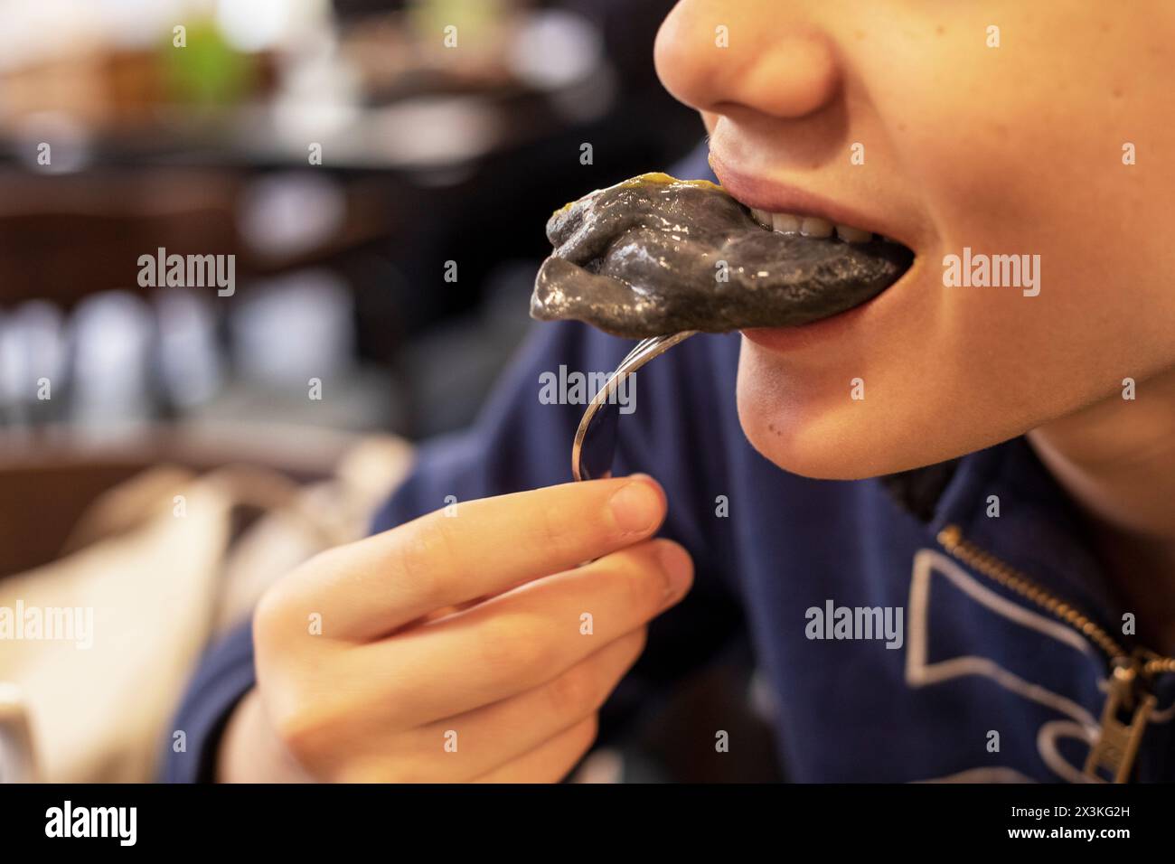 boy bites a black dumpling from a fork. National food Stock Photo