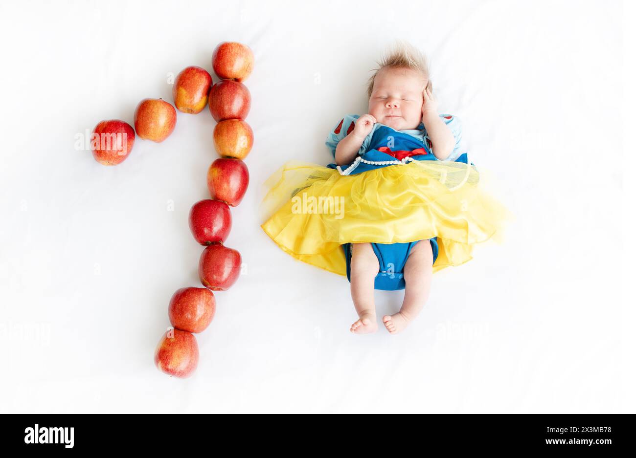 Flat lay picture of a 1 month baby with number made apples. Newborn baby girl in a princess