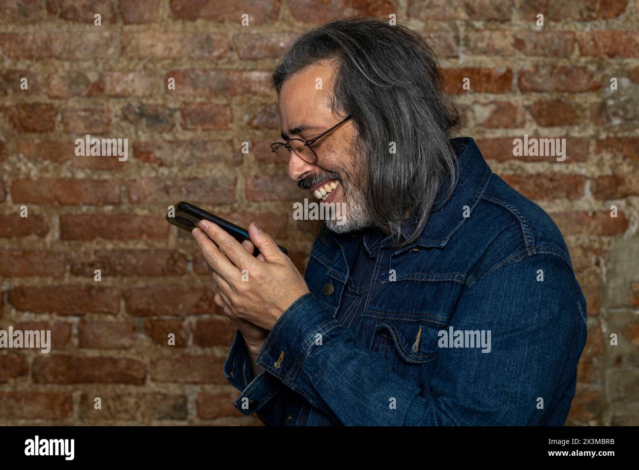 Latin American man (44) with long gray hair smiles while talking on his cell phone. Concept of technology Stock Photo