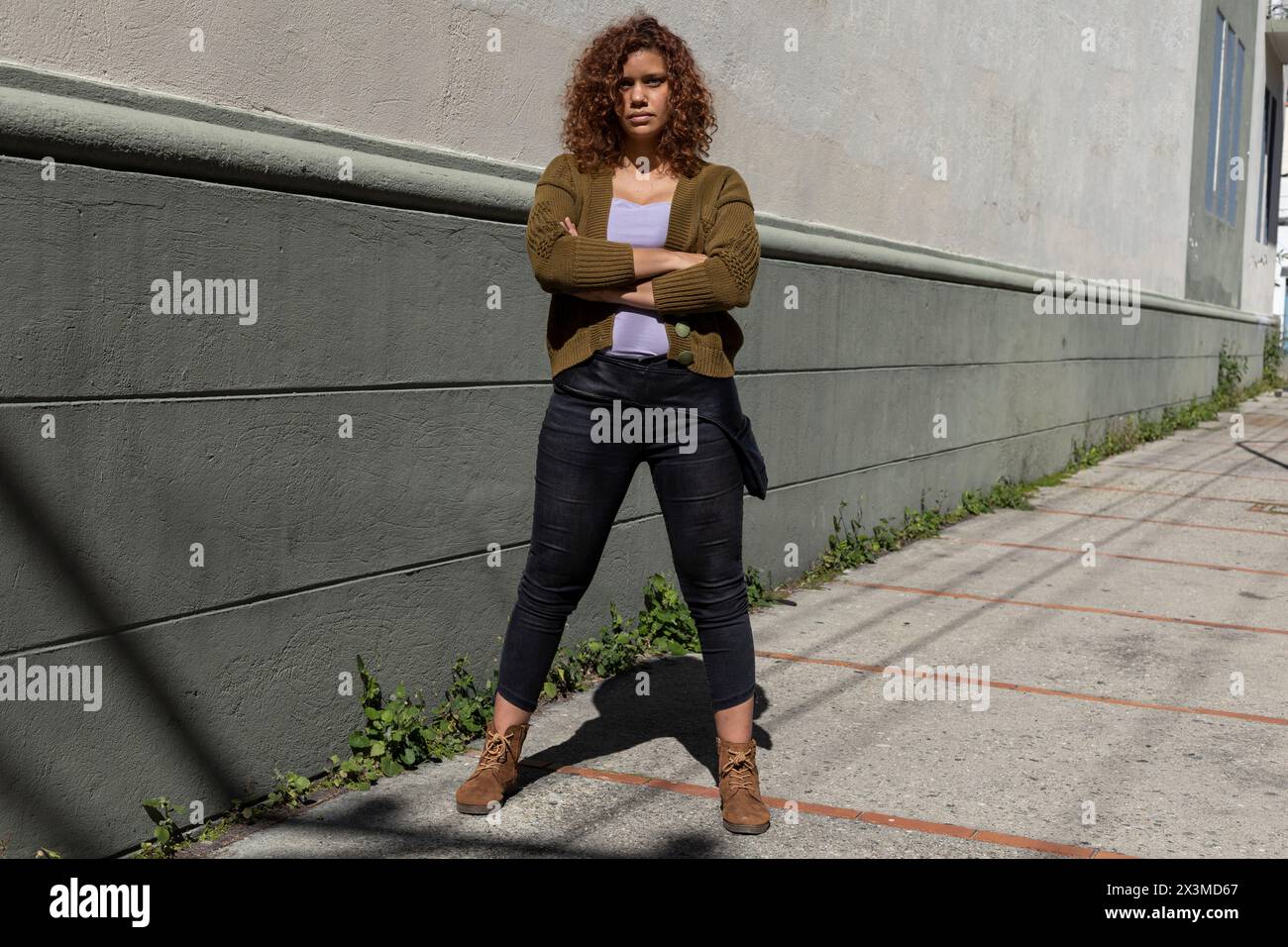 Latin American adult woman (34) of African descent with curly hair poses with arms crossed and serious attitude. Lifestyle concept. Stock Photo