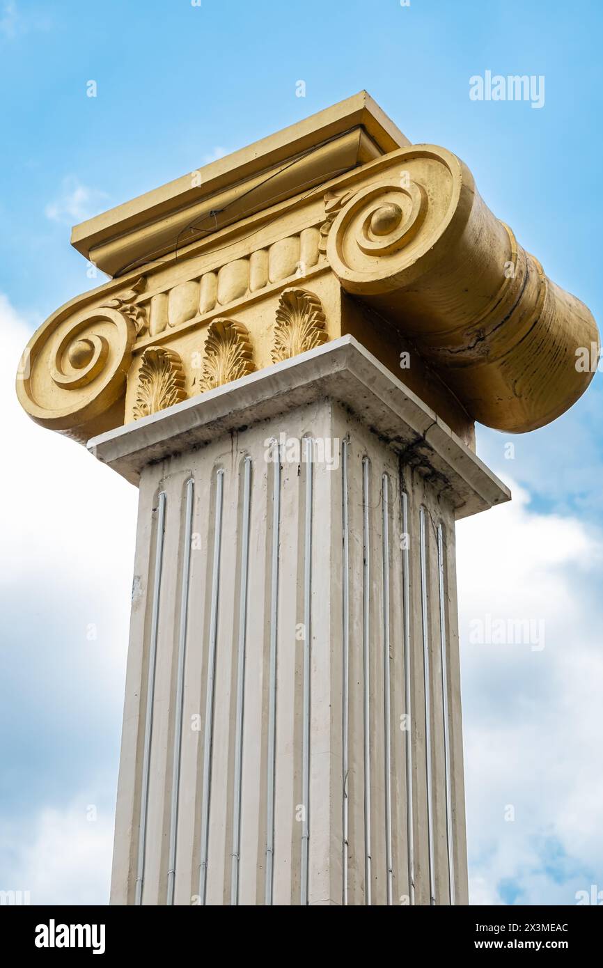 Top part of pillar, Greek-style columns with golden top, exterior detail. Greek-style columns with golden tops against blue sky. Travel photo, nobody Stock Photo