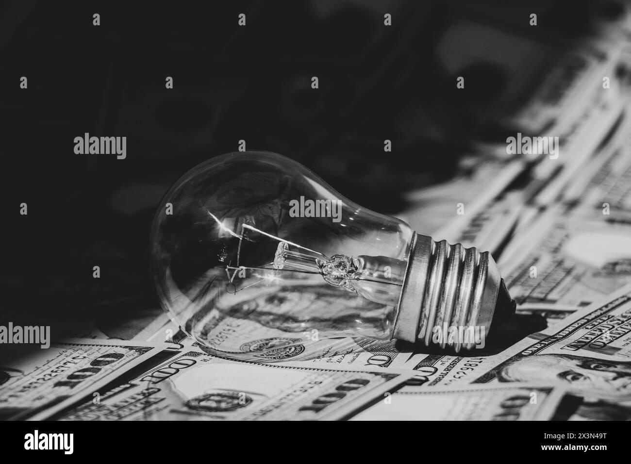 Incandescent lamp lies on dollars in the shade, high price of electricity, business Stock Photo