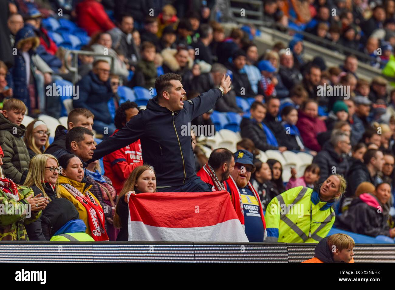 A Middlesbrough FC fan shows his support for his team as he sings passionately with other fans, as a steward looks on. Cardiff City Stadium, Wales. Stock Photo