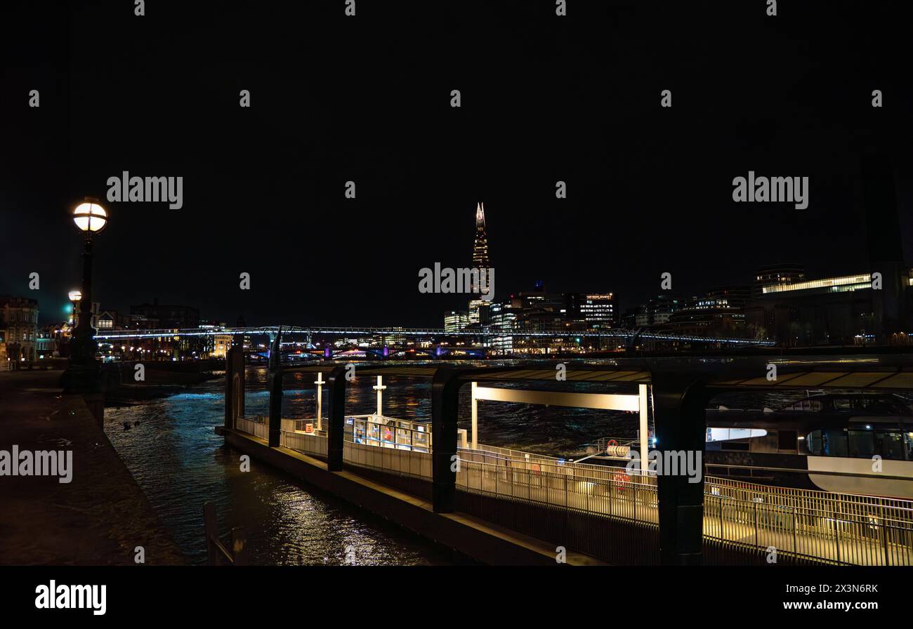 Uber boat dock and walkway, public transportation service along the River Thames, at night with the Millennium Bridge, streetlights and the Shard skys Stock Photo