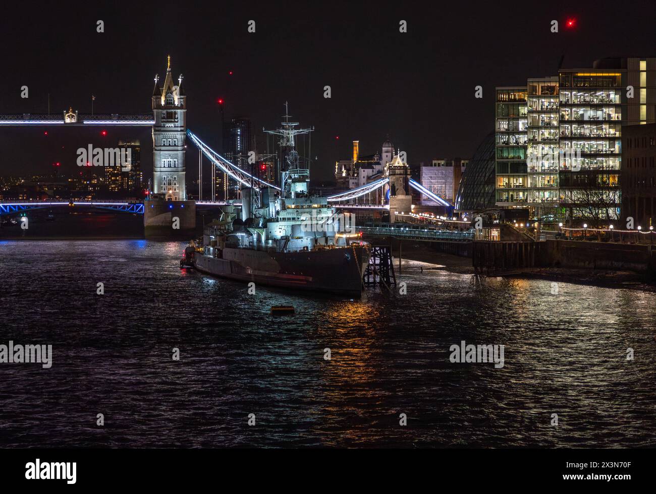 Front view of the war museum ship HMS Belfast docked on the River Thames with reflections of lights from restaurants and buildings in the water in fro Stock Photo