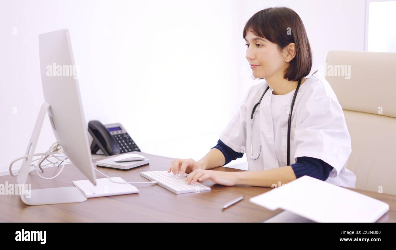 Doctor using computer sitting on a desk in a clinic Stock Photo