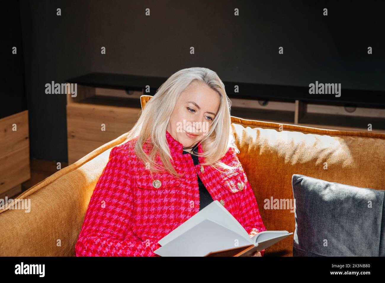 Mature lady engrossed in a novel, relaxed on a mustard couch Stock ...