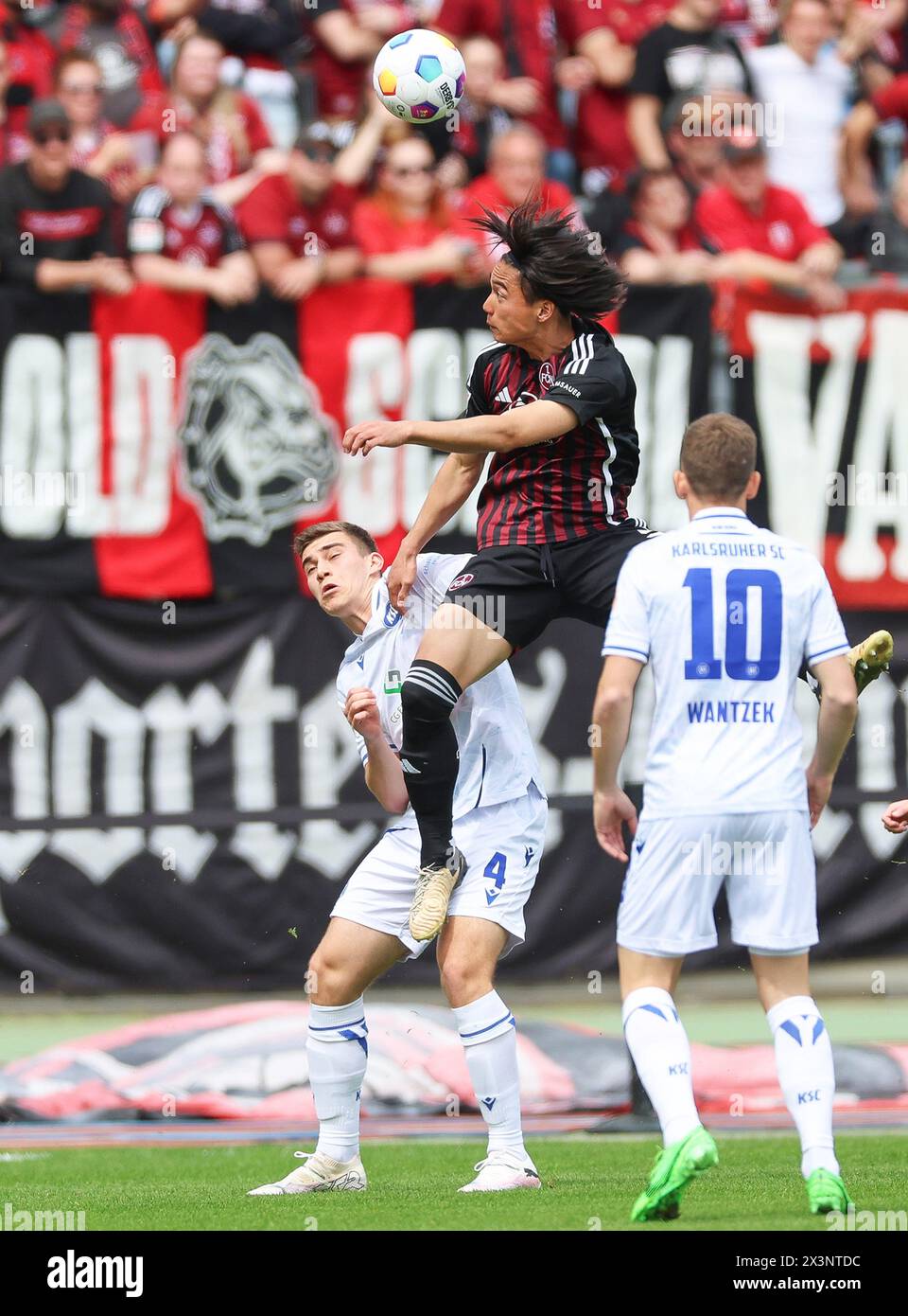 Nuremberg, Germany. 28th Apr, 2024. Soccer: Bundesliga 2, 1. FC Nürnberg - Karlsruher SC, Matchday 31, Max-Morlock-Stadion. Nuremberg's Daichi Hayashi (M) goes up for a header against Karlsruhe's Marcel Beifus (l). Credit: Daniel Löb/dpa - IMPORTANT NOTE: In accordance with the regulations of the DFL German Football League and the DFB German Football Association, it is prohibited to utilize or have utilized photographs taken in the stadium and/or of the match in the form of sequential images and/or video-like photo series./dpa/Alamy Live News Stock Photo