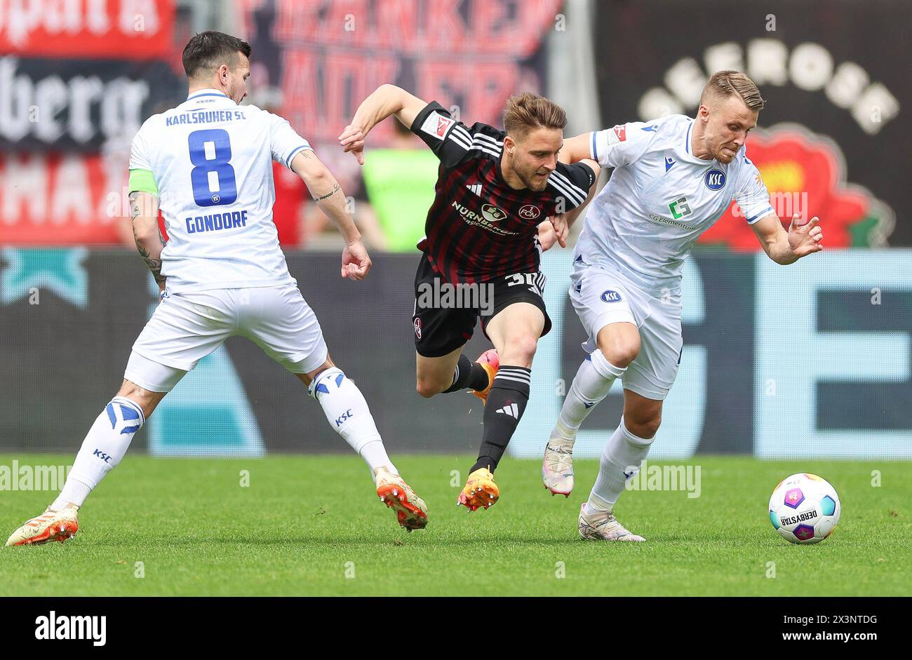 Nuremberg, Germany. 28th Apr, 2024. Soccer: Bundesliga 2, 1. FC Nürnberg - Karlsruher SC, Matchday 31, Max-Morlock-Stadion. Nuremberg's Lukas Schleimer (center) in action against Karlsruhe's players Marco Thiede (right) and Jerome Gondorf. Credit: Daniel Löb/dpa - IMPORTANT NOTE: In accordance with the regulations of the DFL German Football League and the DFB German Football Association, it is prohibited to utilize or have utilized photographs taken in the stadium and/or of the match in the form of sequential images and/or video-like photo series./dpa/Alamy Live News Stock Photo