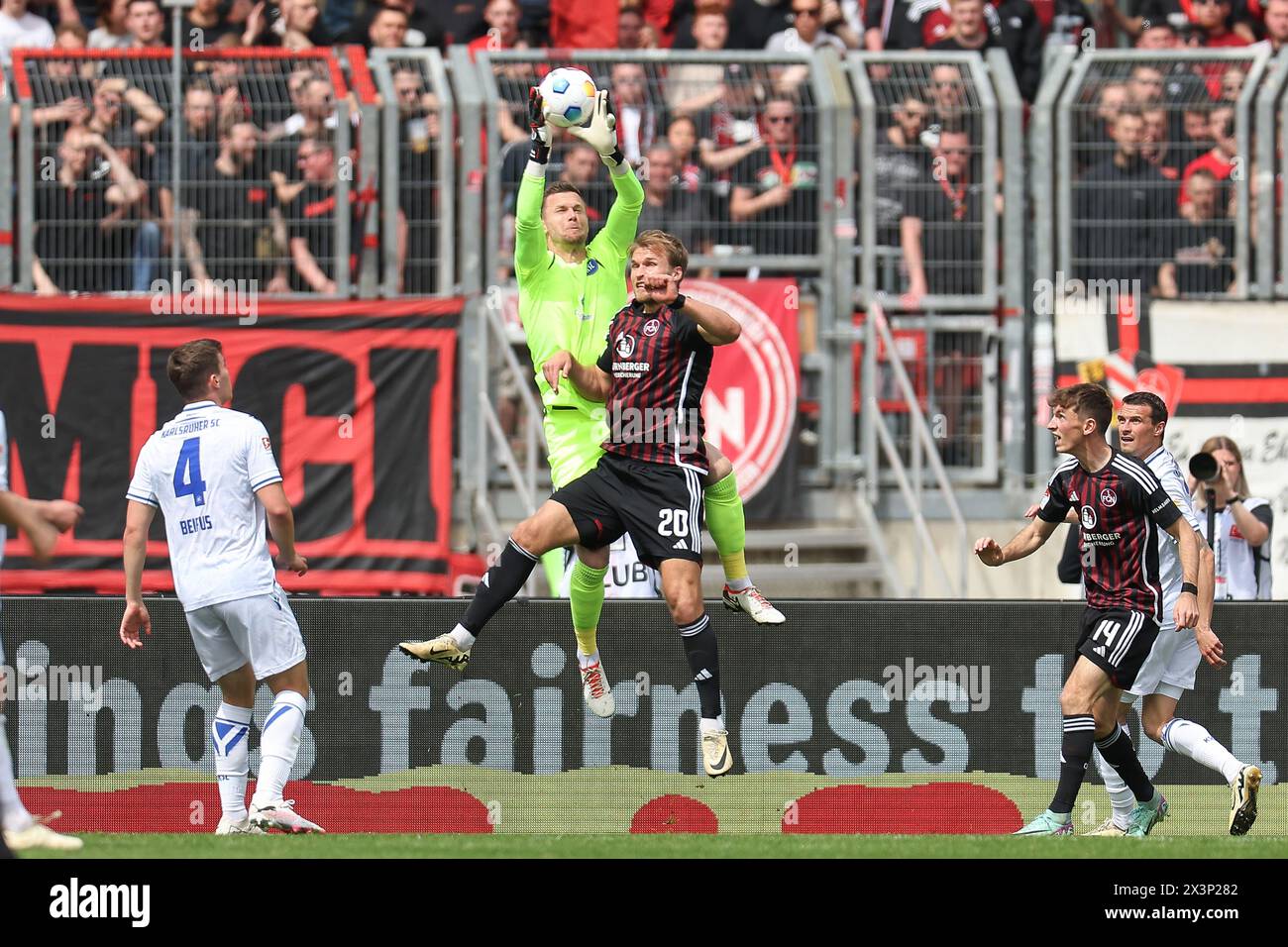 Nuremberg, Germany. 28th Apr, 2024. Soccer: Bundesliga 2, 1. FC Nürnberg - Karlsruher SC, Matchday 31, Max-Morlock-Stadion. Karlsruhe goalkeeper Patrick Drewes (center l) clears the ball in front of Nuremberg's Martin Sebastian Anderson (center r). Credit: Daniel Löb/dpa - IMPORTANT NOTE: In accordance with the regulations of the DFL German Football League and the DFB German Football Association, it is prohibited to utilize or have utilized photographs taken in the stadium and/or of the match in the form of sequential images and/or video-like photo series./dpa/Alamy Live News Stock Photo