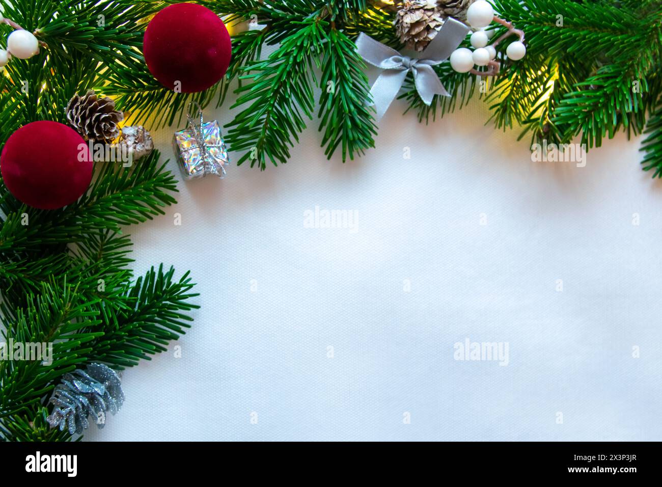 White background and Christmas tree spruce for frame with gifts, red ball, white berries, cones. Copy space. Top view. Stock Photo