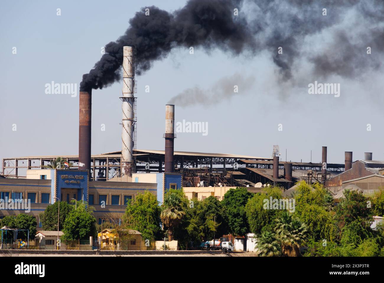 Sugar mill factory belching black smoke pollution from its chimneys. Near Esna, Egypt Stock Photo