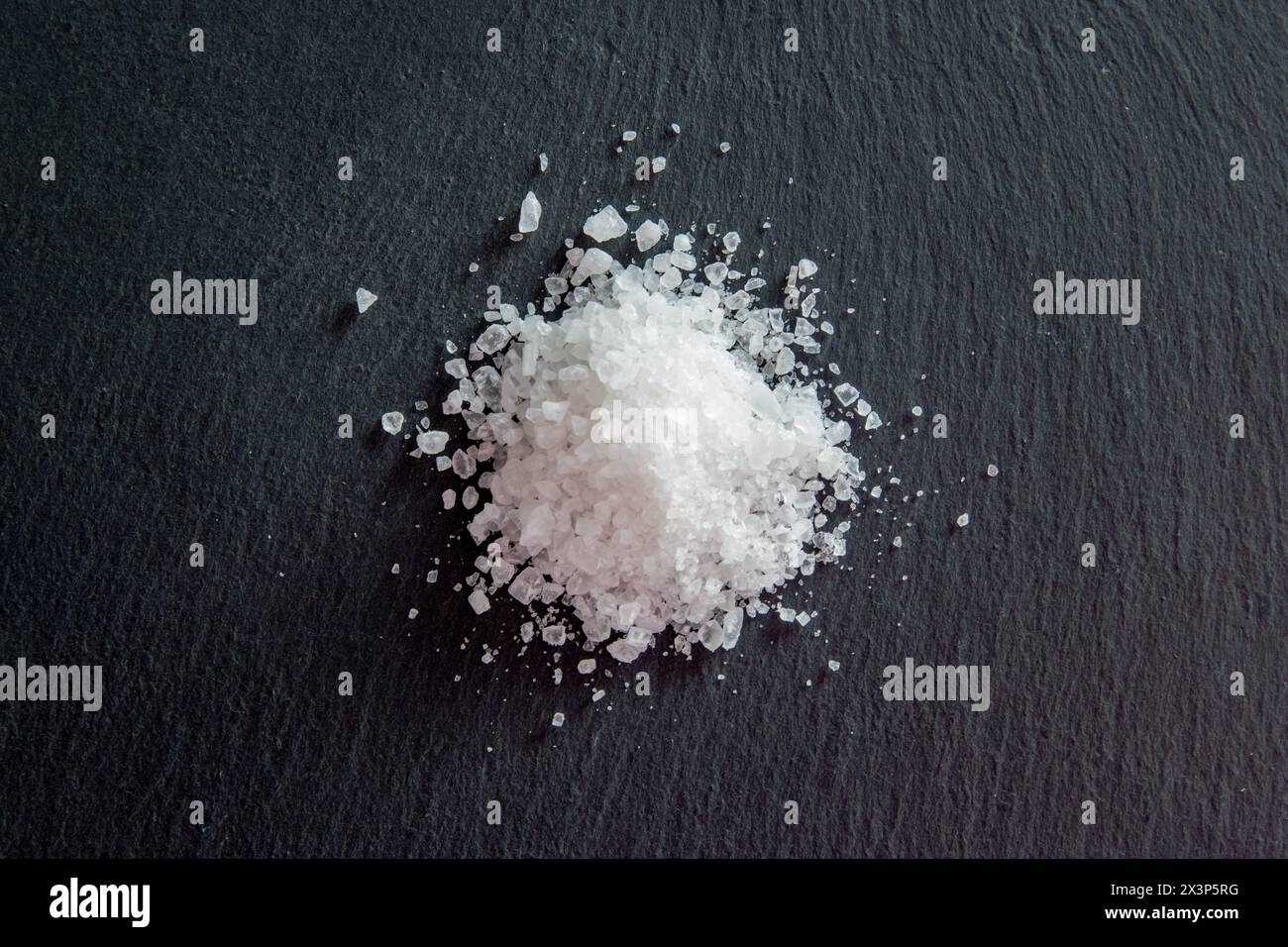 White salt cristals for food on the black natural background. Salt crystals for cooking. Stock Photo