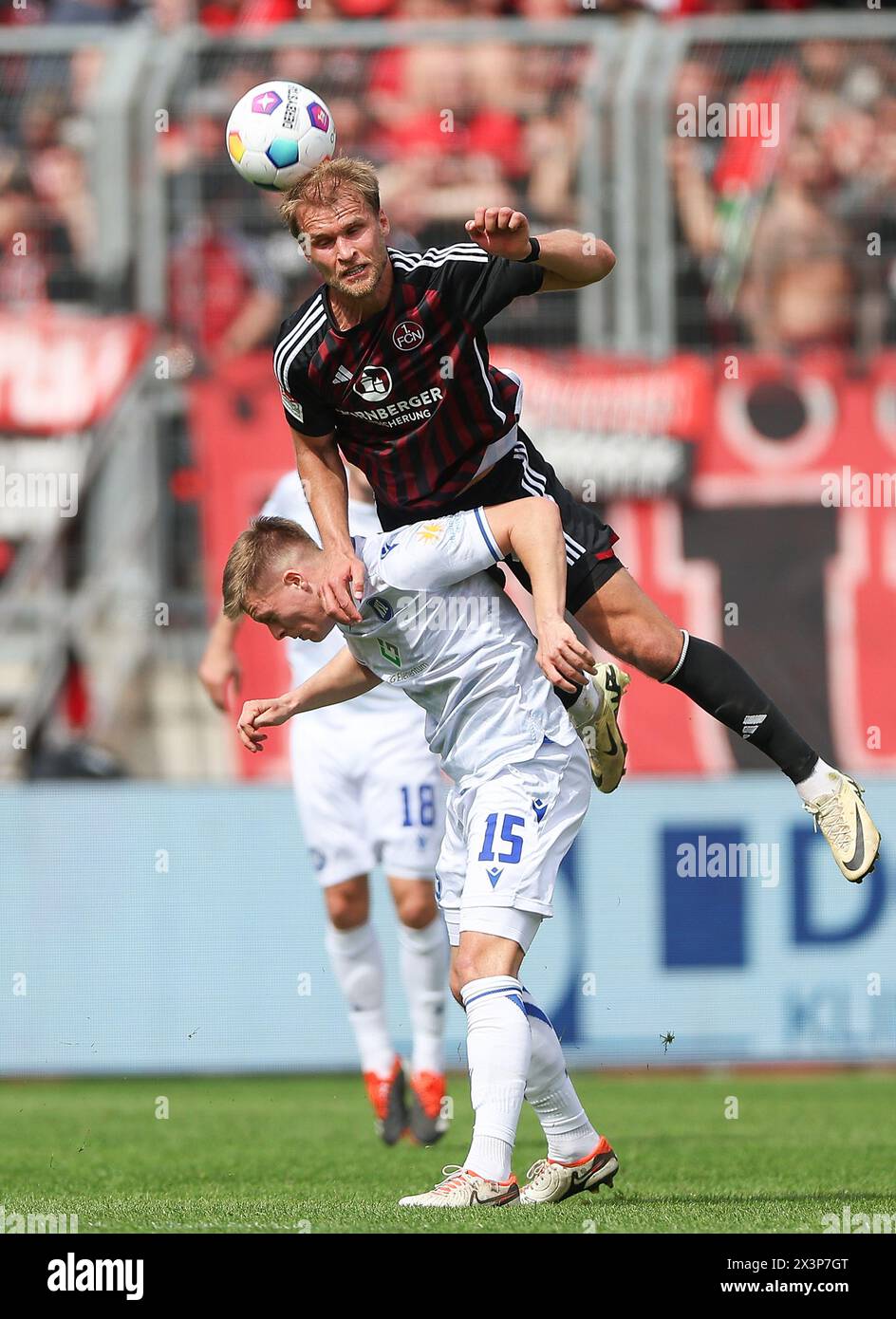 Nuremberg, Germany. 28th Apr, 2024. Soccer: Bundesliga 2, 1. FC Nürnberg - Karlsruher SC, Matchday 31, Max-Morlock-Stadion. Nuremberg's Martin Sebastian Anderson (above) goes up for a header against Karlsruhe's Dzenis Burnic. Credit: Daniel Löb/dpa - IMPORTANT NOTE: In accordance with the regulations of the DFL German Football League and the DFB German Football Association, it is prohibited to utilize or have utilized photographs taken in the stadium and/or of the match in the form of sequential images and/or video-like photo series./dpa/Alamy Live News Stock Photo