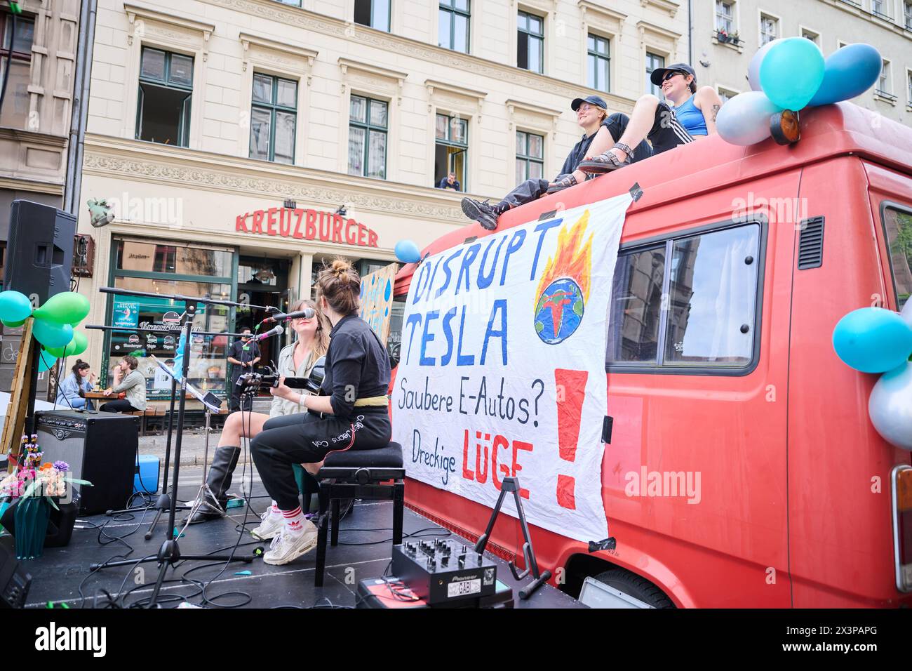 28 April 2024, Berlin: 'Disrupt Tesla - Clean e-cars? Dirty lie!' is written on a banner hanging from a minibus. Members of various alliances such as 'Tesla den Hahn abdrehen', 'A100 stoppen!' and 'Görlitz zaunfrei!' are celebrating a street party in Kreuzberg to demonstrate against Tesla and car policy. Photo: Annette Riedl/dpa Stock Photo
