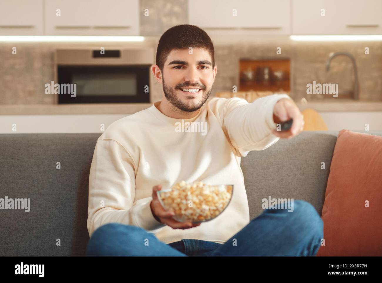Man Sitting on Couch Holding Bowl of Popcorn, Watching TV Stock Photo