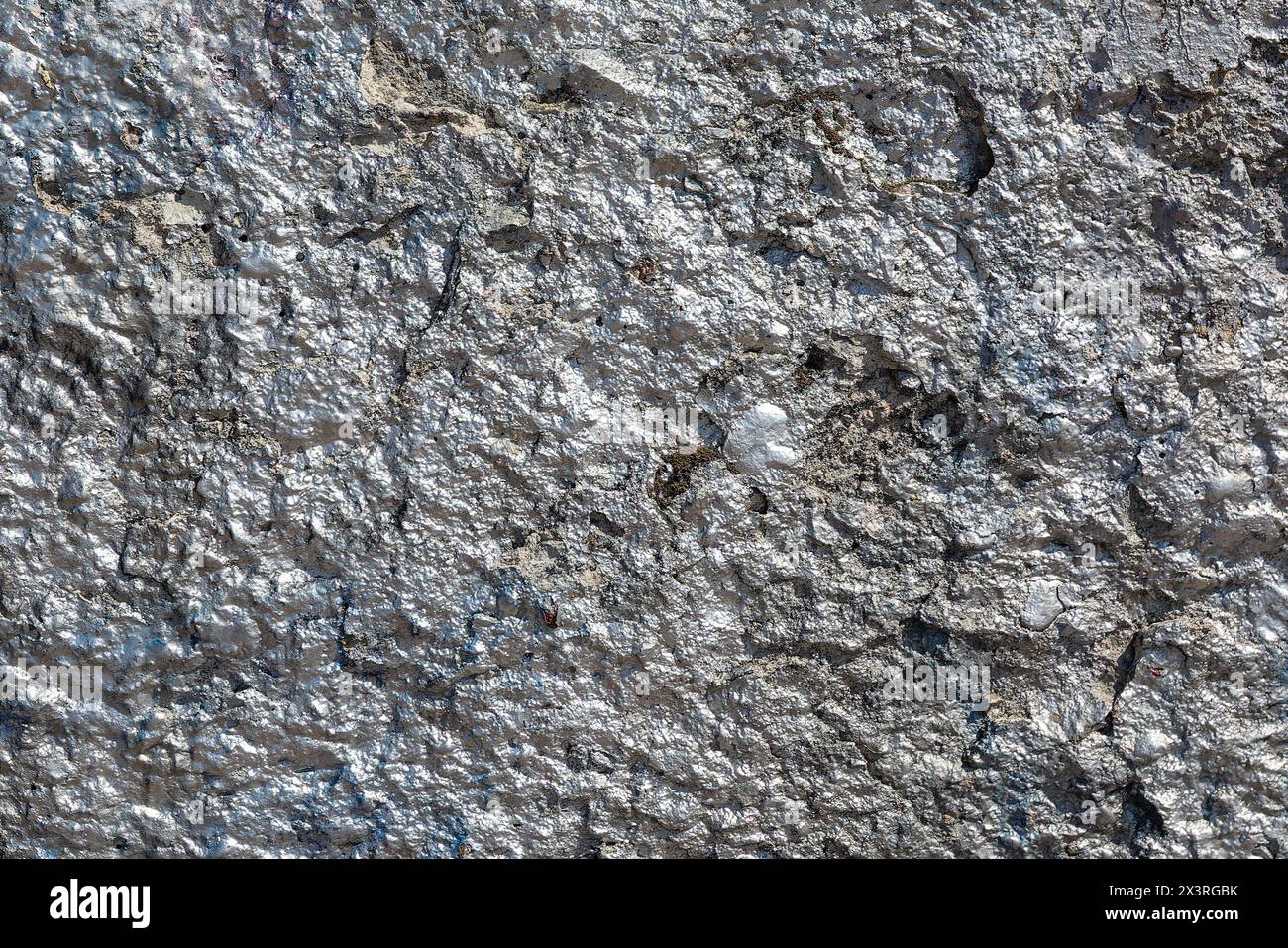 The nice, old rough and cracked concrete wall is painted with silver shining paint. Stock Photo