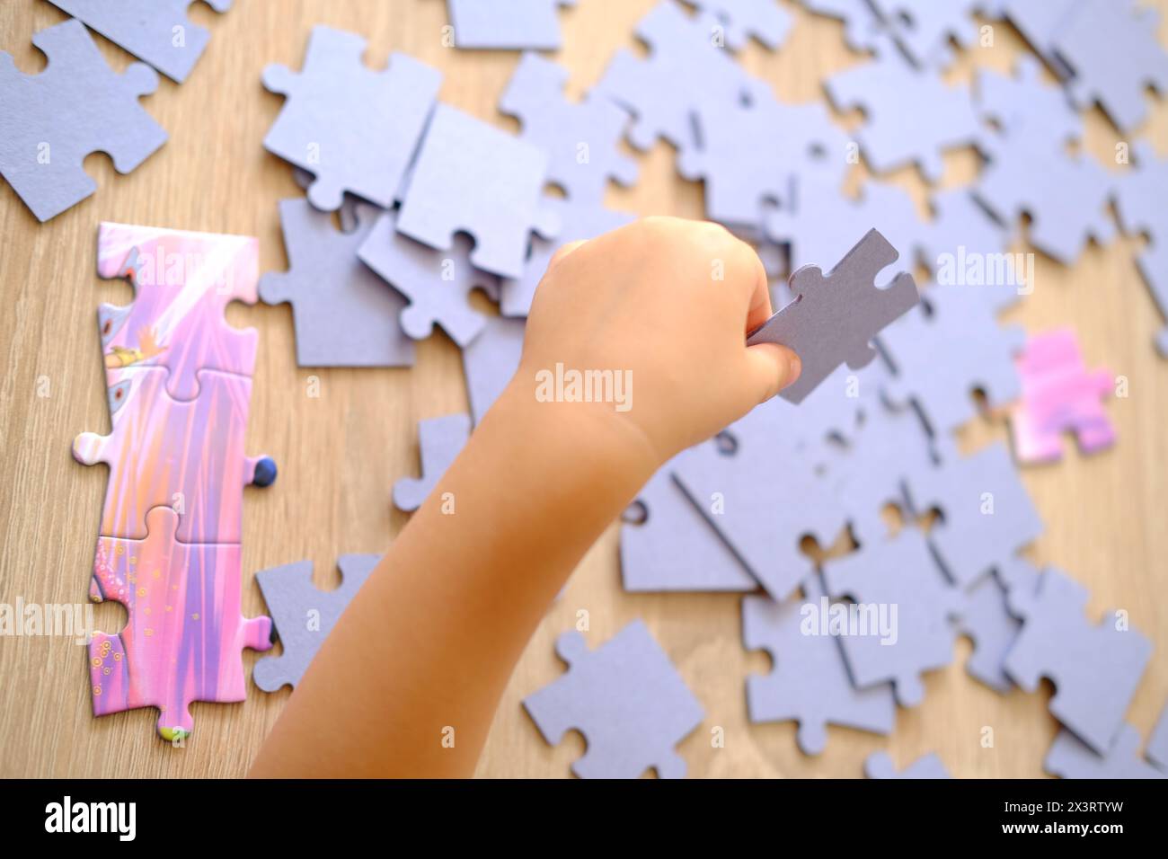 little child is assembling puzzles, sorting cardboard pieces by shape