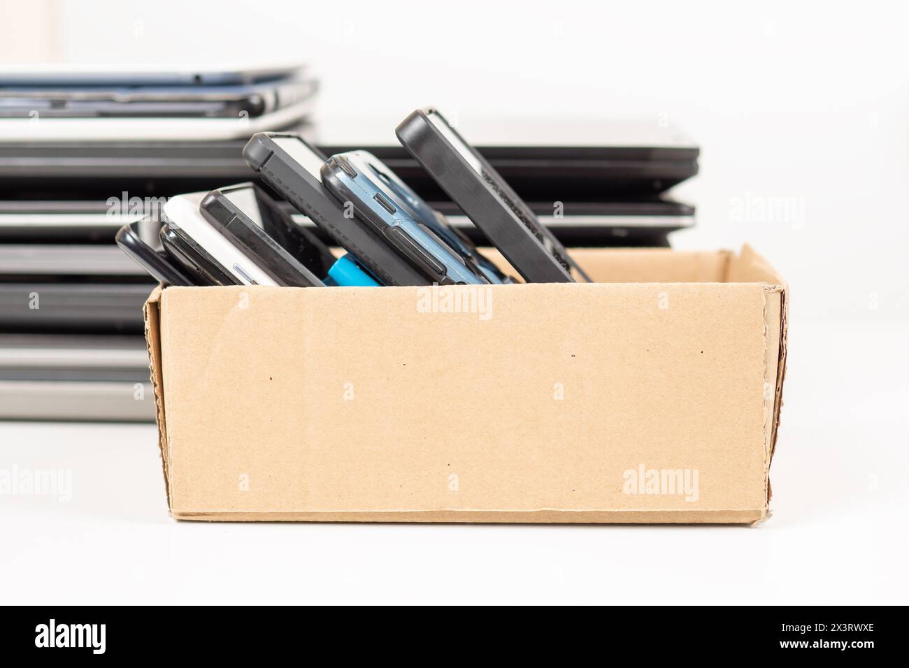 Box with used smartphones and pile of old laptop computers, digital tablets for recycling on table. Donation box, technology to charity, e-waste, elec Stock Photo