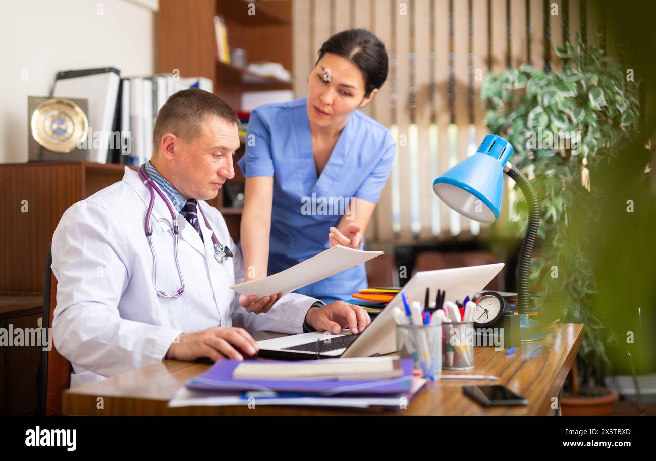 Two focused physicians working with case histories on laptop Stock Photo
