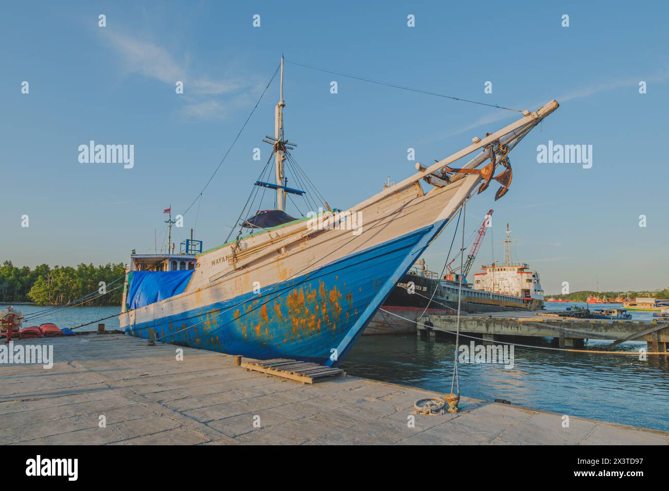 Balikpapan, Indonesia - April 12th, 2024. a classic blue and white Bugis schooner boat docked at a pier. The boat has a cabin with white trim and wind Stock Photo