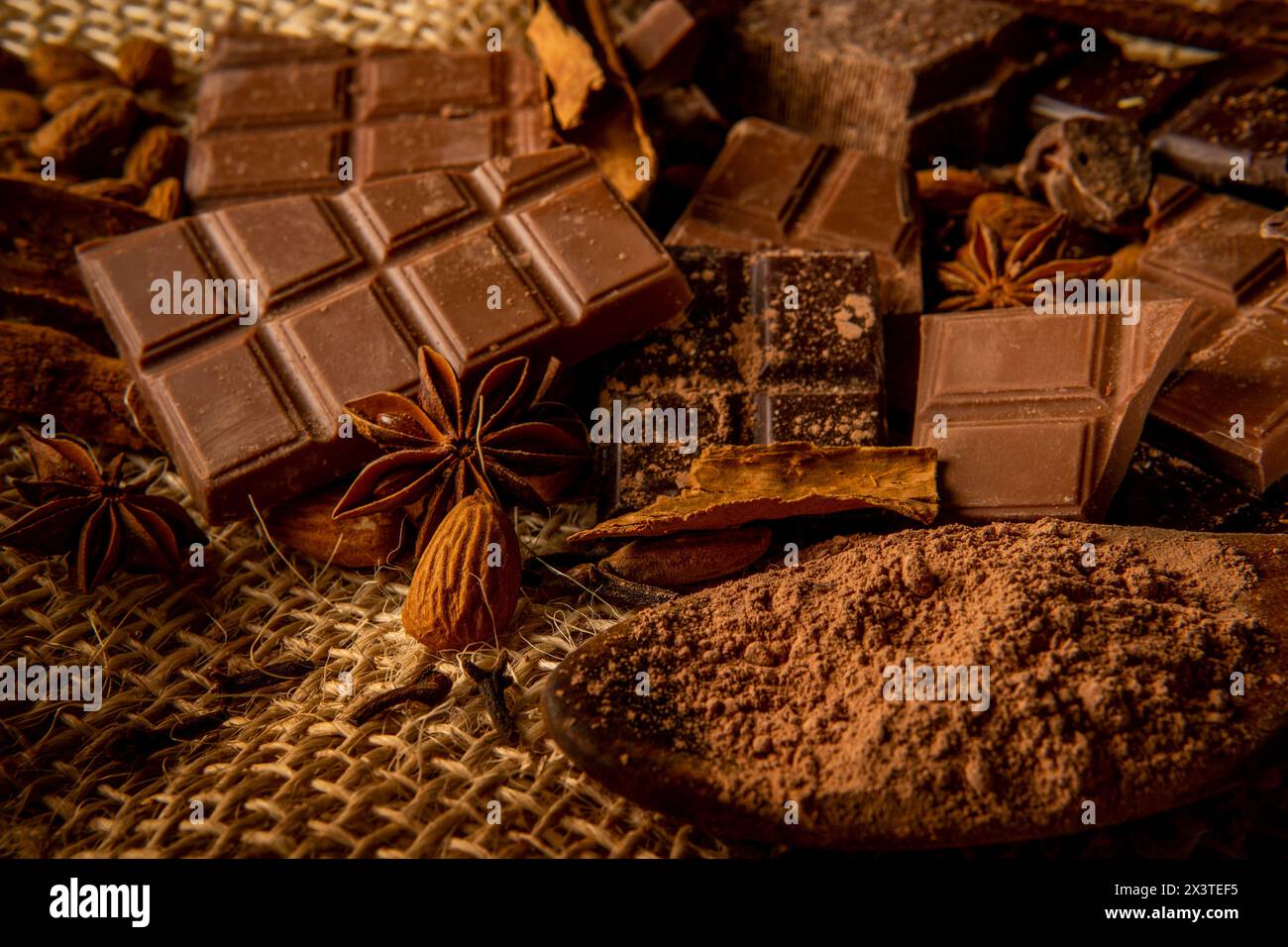 Still life with pieces of variety of chocolate and spices such as cinnamon, star anise and almonds on a jute background Stock Photo