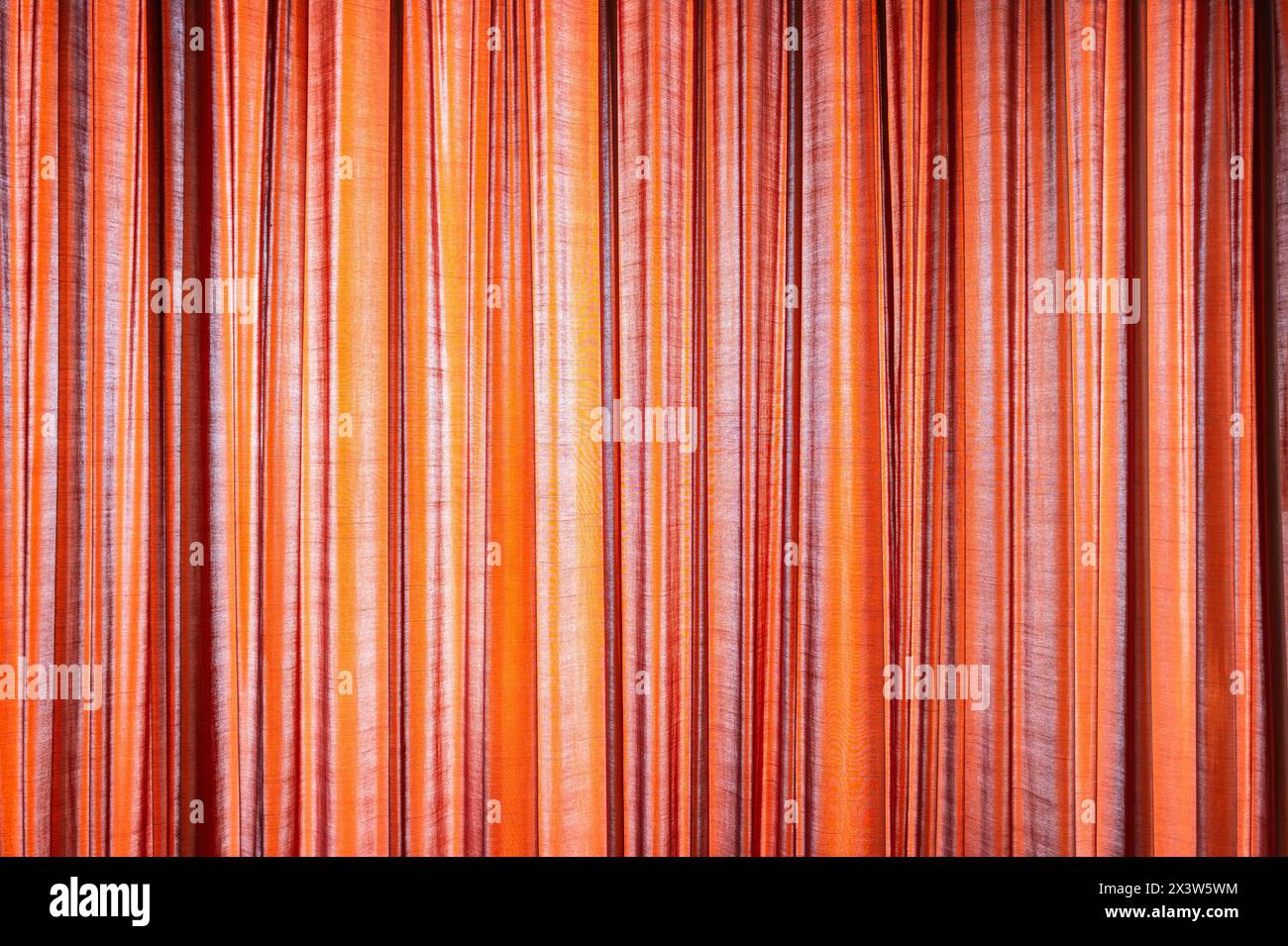 Background of orange stripped curtain covering window with bright sunlight outside. Stock Photo