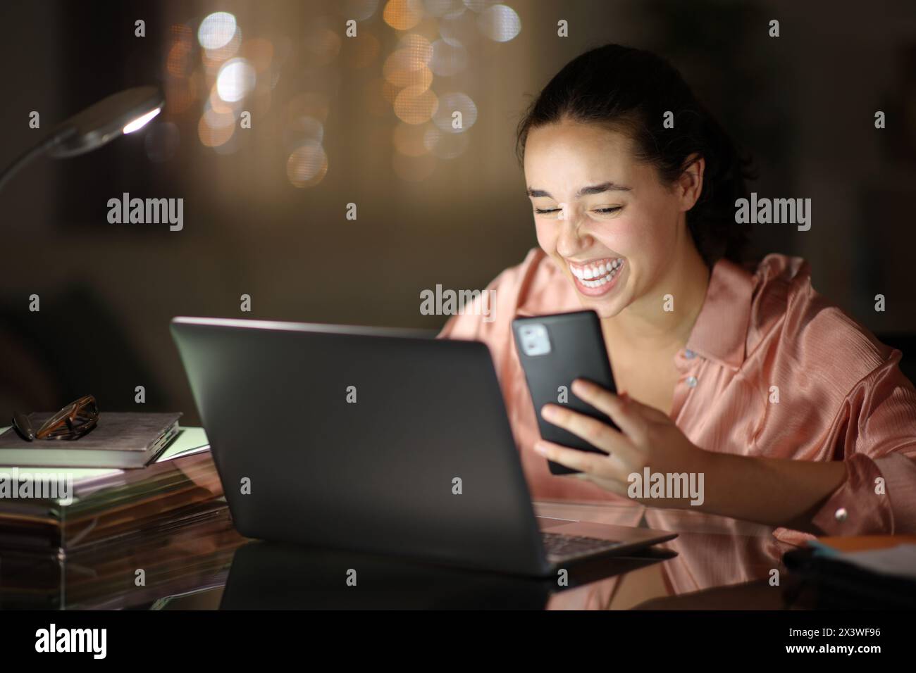 Happy tele worker in the night laughing hilariously checking phone at home Stock Photo