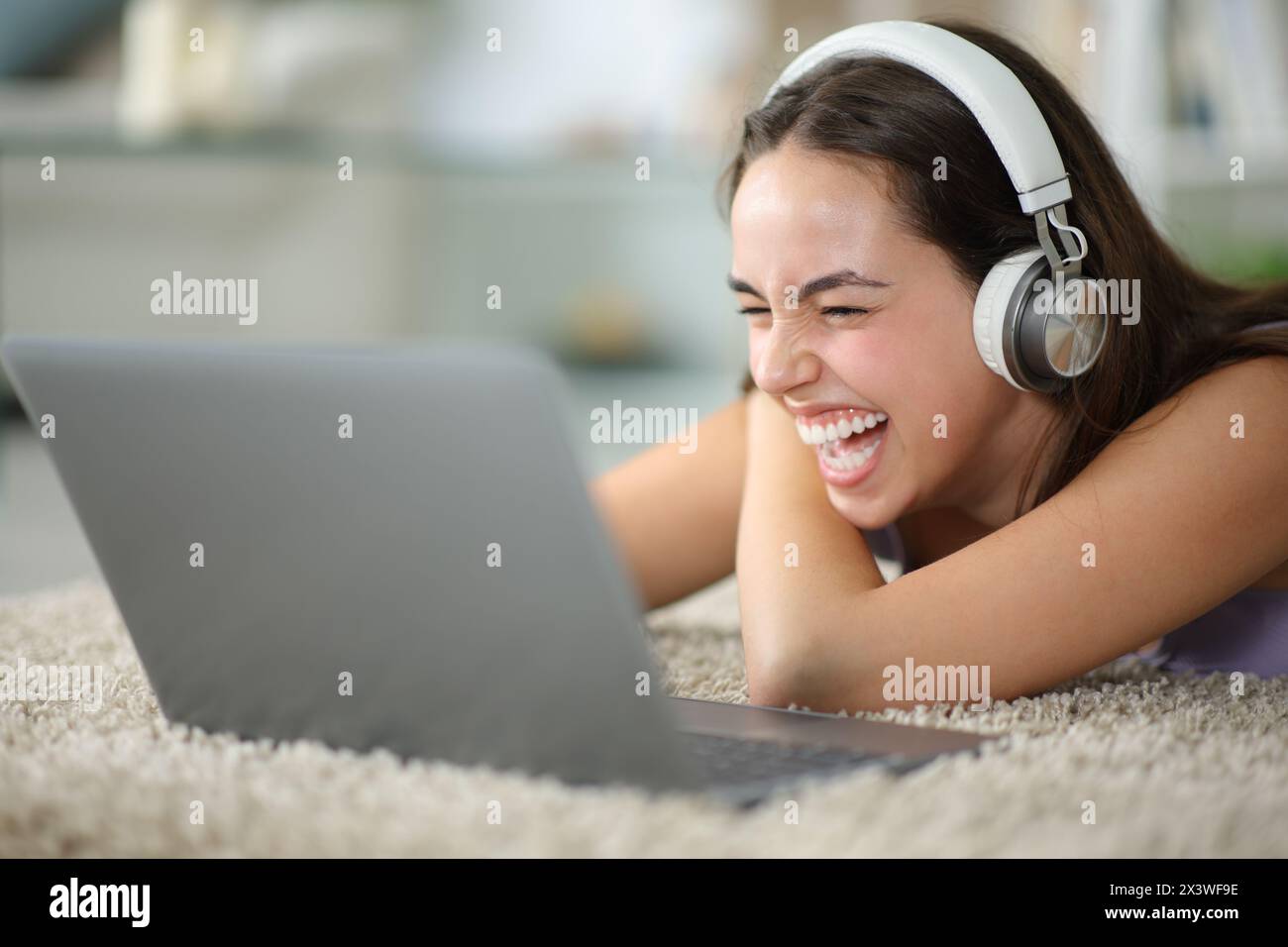 Happy woman watching media and laughing lying on the floor at home Stock Photo