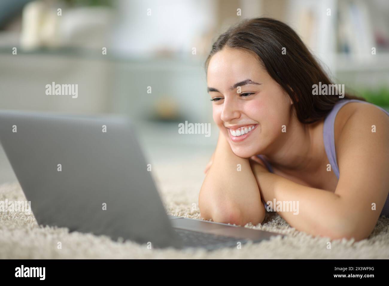 Happy woman lying on the floor watching media on laptop at home Stock Photo